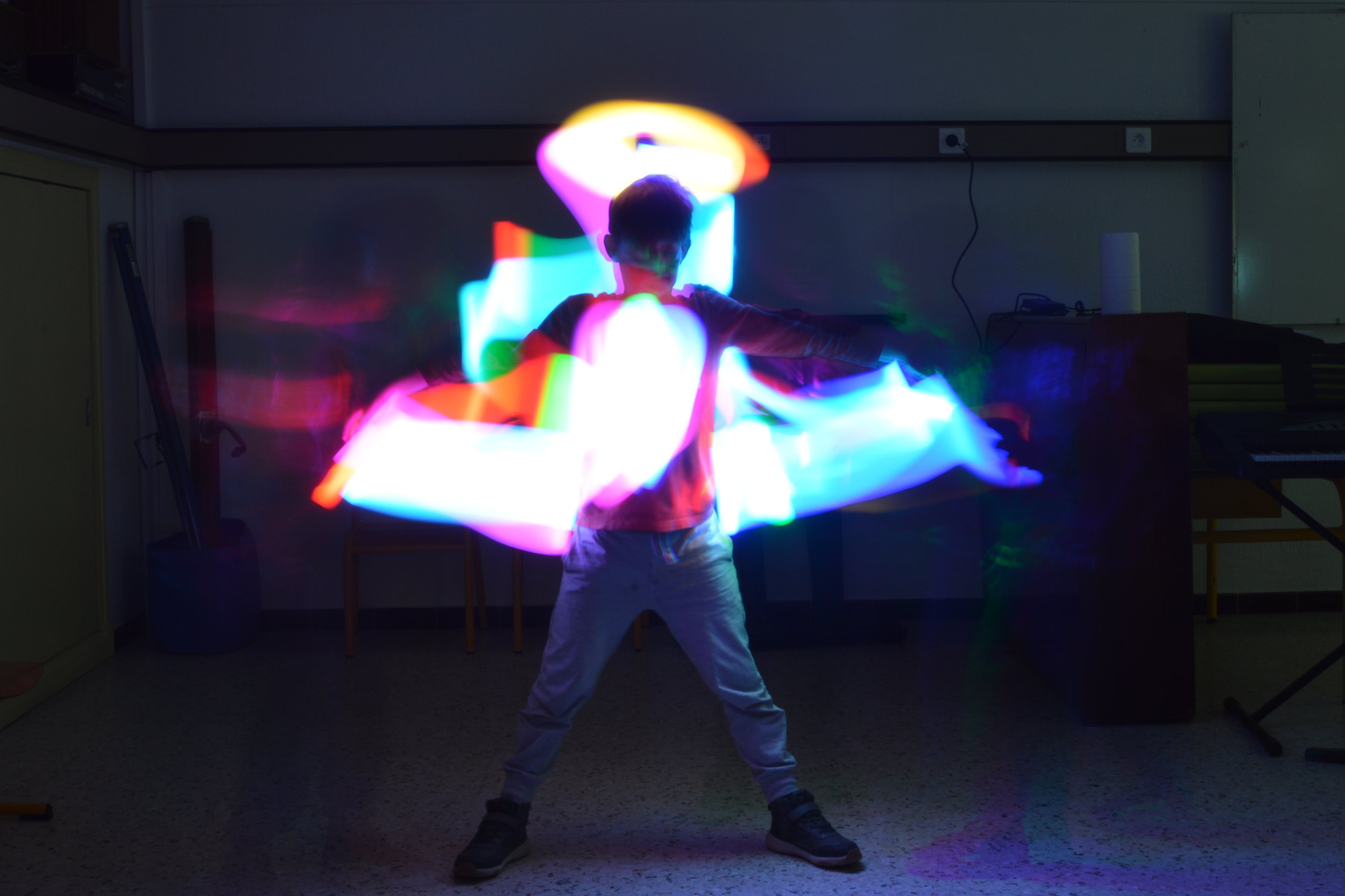 Un enfant qui danse avec des lumières LED colorées dans une pièce sombre, créant un effet lumineux autour de lui.