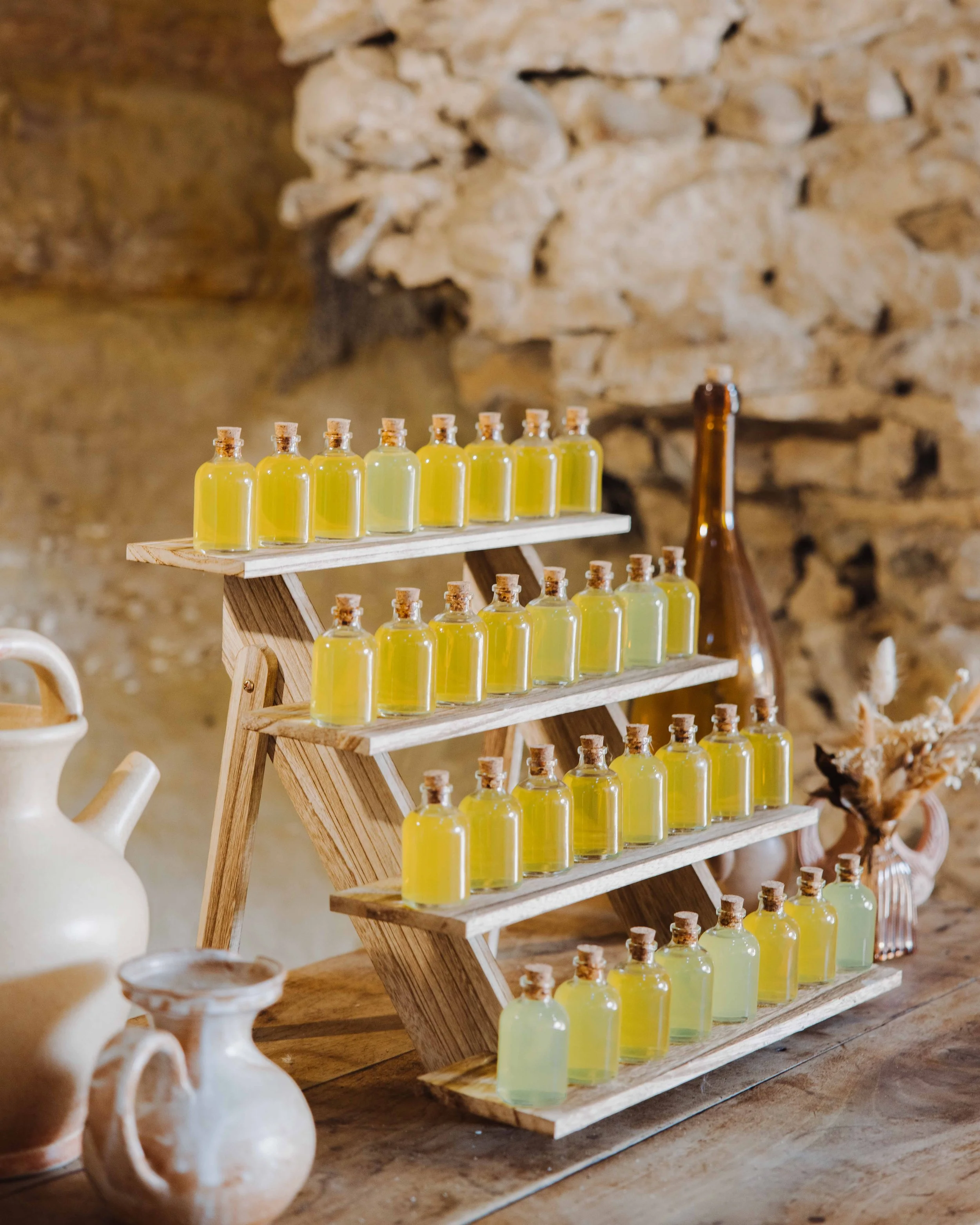 Étagère en bois avec plusieurs petites bouteilles de couleur jaune et verte, échangeant des liquides, dans un cadre rustique avec poteries et décorations Photographe mariage Isère, ferme du rocher, cérémonie civil et laïque. Bordeaux et Lyon.