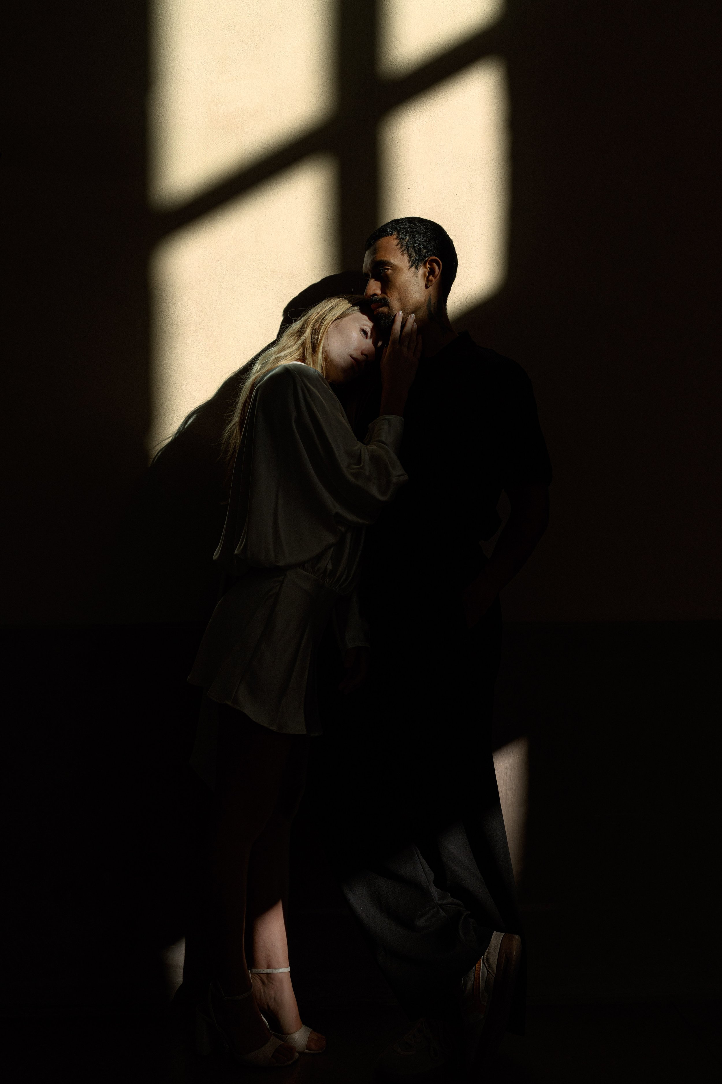 Deux personnes dans une pièce sombre avec des reflets de lumière sur un mur, l'une d'elles repose sa tête sur l'autre, créant une atmosphère intime à l'hôtel dieu à Lyon 2ème, à l'intercontinental, session engament, photographe mariage duo 