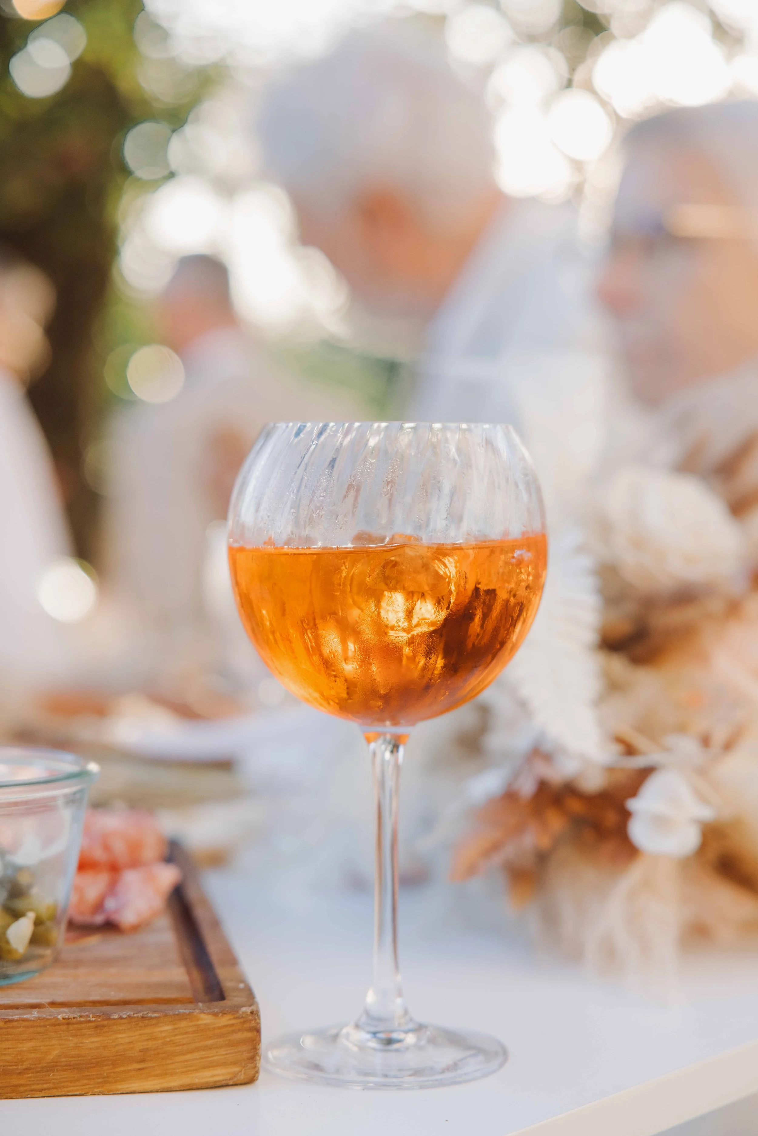 Verre à vin rosé sur une table lors d'une fête en extérieur, décorée avec des éléments naturels. Mariage à la ferme du rocher en Isère, cocktails de mariage, spritz.  Photographe en duo haut de gamme et destination wedding.