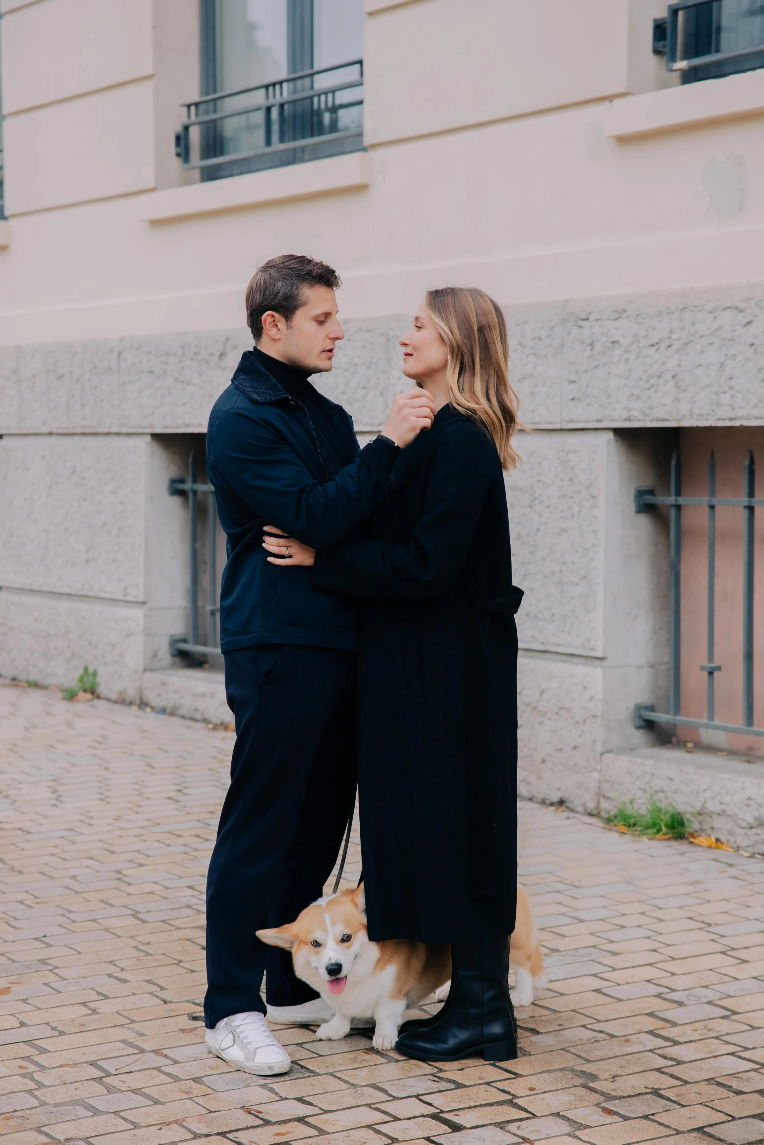 Un couple regarde tendrement dans la rue, avec un chien corgi entre eux. session engagement couple Lyon 6eme, brotteaux, photographe mariage bordeaux et Lyon et destination wedding