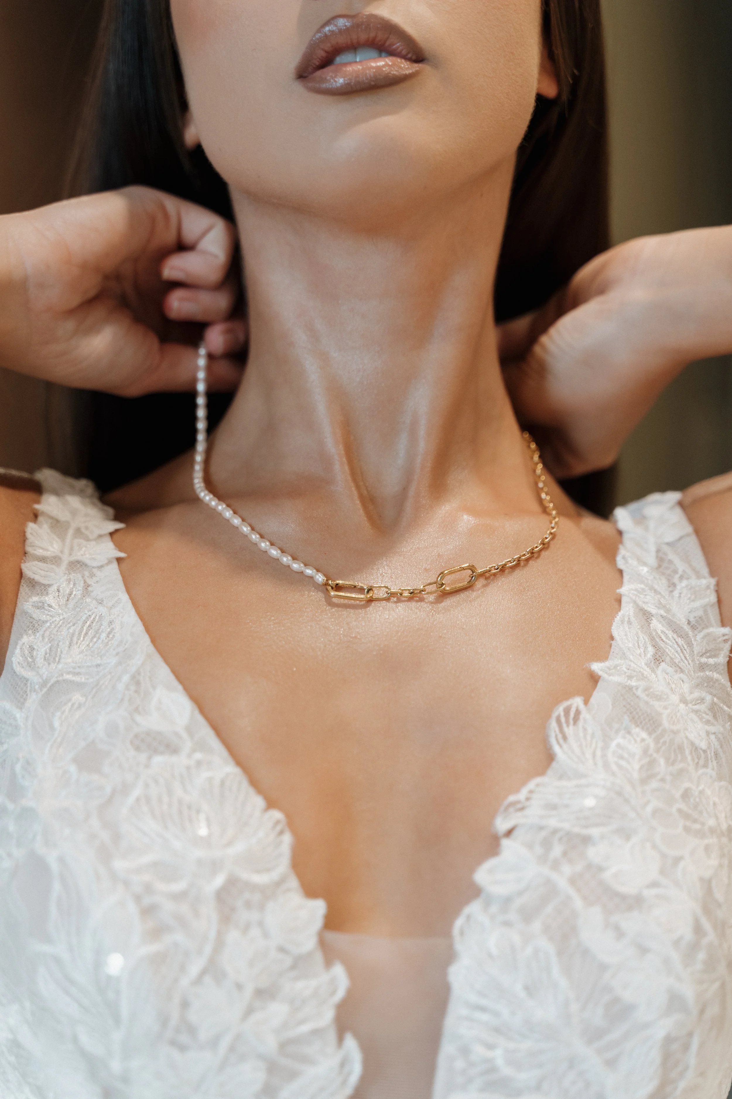 Gros plan sur un collier porté par une femme, entre perles blanches et maillons en or, avec robe en dentelle blanche.  session femme mariées et robes haut de gamme, brindos, hôtel et lac,  photographe mariage bordeaux et Lyon et destination wedding