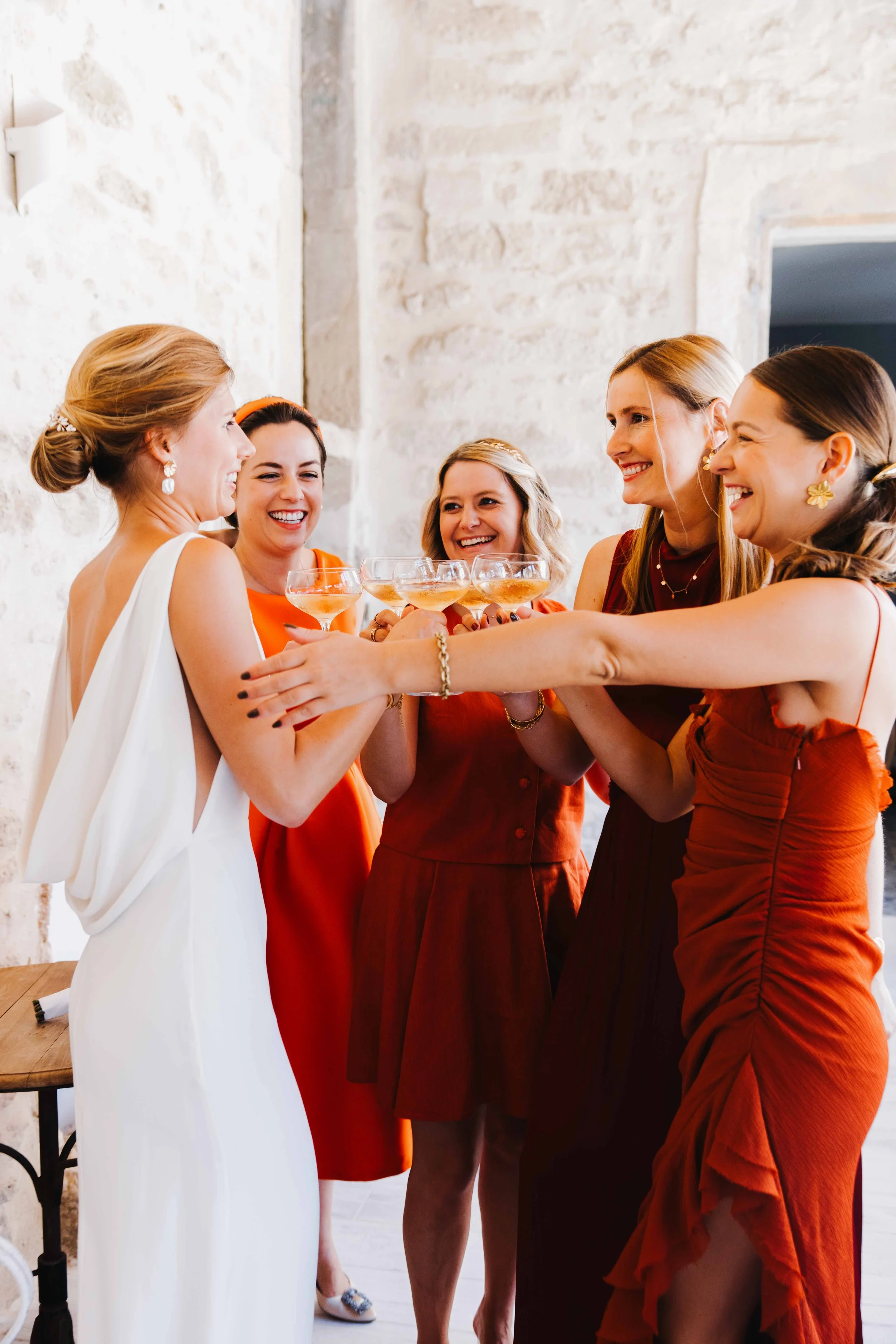 Des femmes souriantes au mariage, levant ensemble des verres à l'apéritif. Domaine du bijoutier à grignan, drome provençal, coucher de soleil, session couple, mariage religieux, cérémonie religieuse, champagne, demoiselles d'honneurs 
