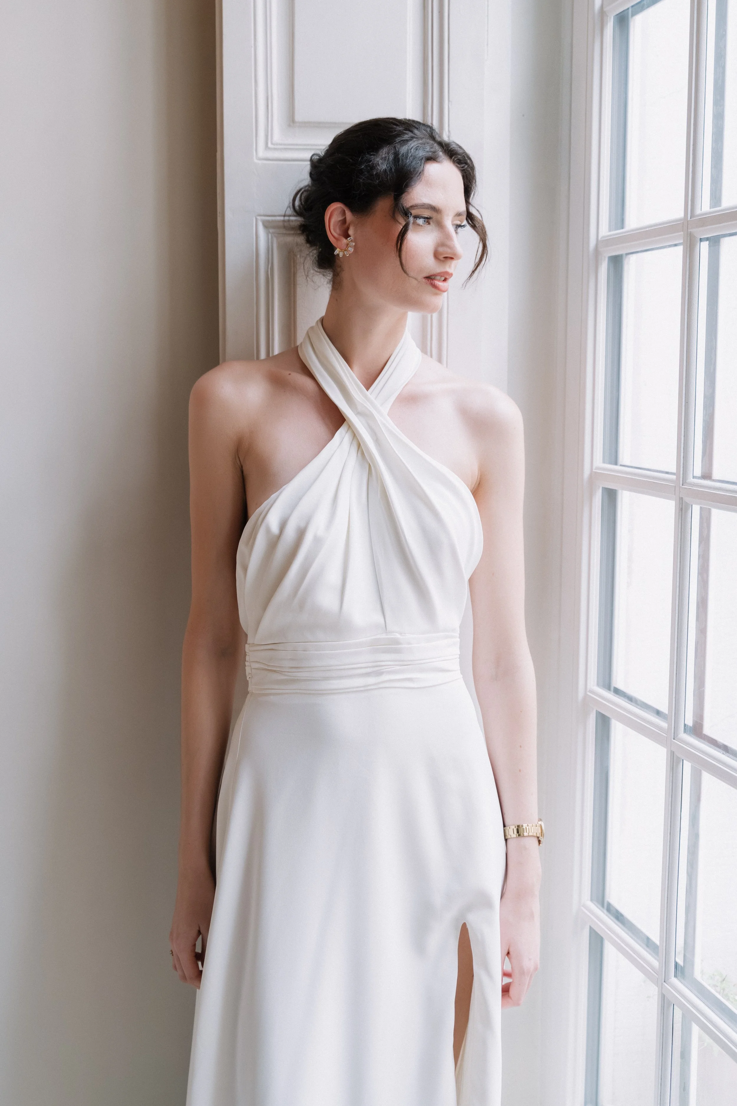 Une femme porte une robe blanche élégante, debout près d'une fenêtre, regardant à l'extérieur. Session engagement paris, Louvre, mariage haut de gamme, destination wedding. Robe de mariées, madame a dit oui
