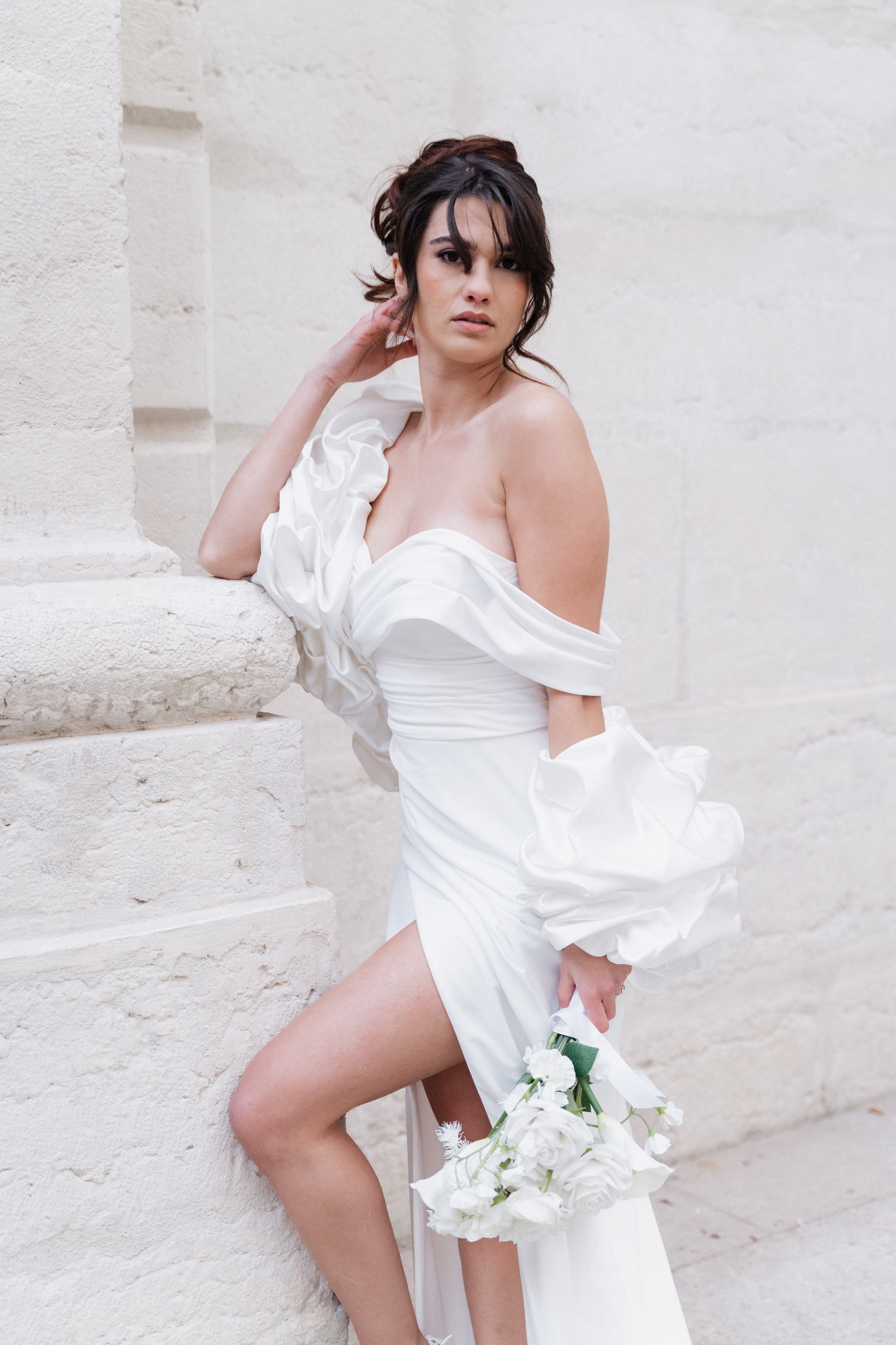 Jeune femme en robe de mariage blanche posant contre un mur en pierre, tenant un bouquet de fleurs blanches à l'hôtel dieu à Lyon 2ème, à l'intercontinental, session engament.