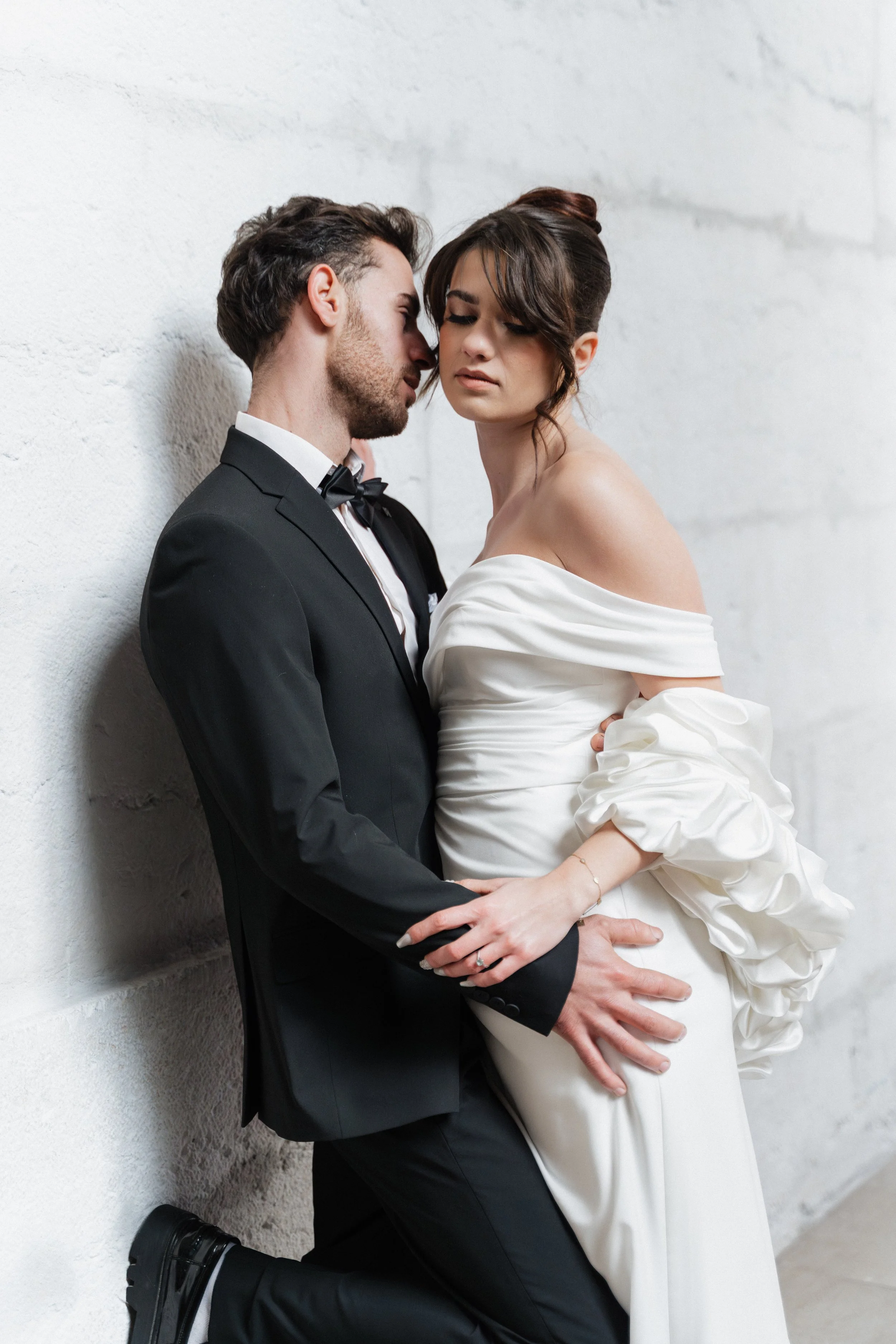 Un couple en tenue de mariage posant contre un mur blanc, dans une ambiance élégante et romantique à Lyon 2ème à l'hôtel dieu à l'intercontinental lors d'une session engagement par un duo de photographe de mariage et de sessions couples 