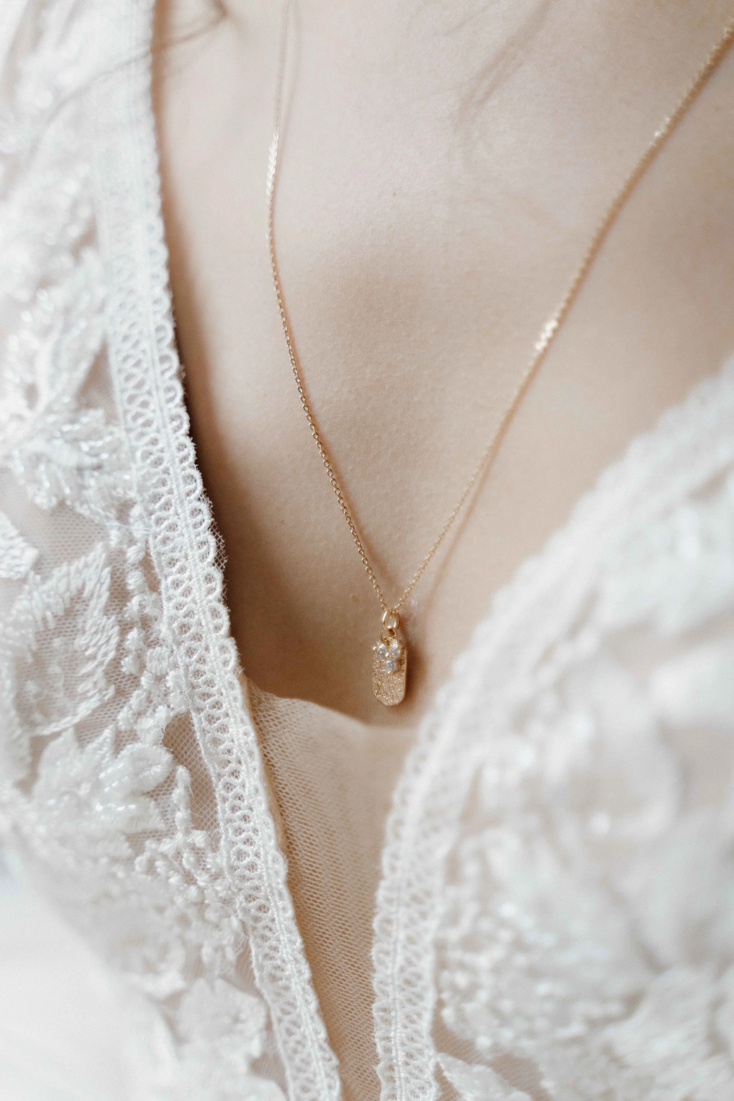 Collier en or avec pendentif en forme de capsule, porté sur un décolleté en dentelle blanche de vêtement de mariage ou de cérémonie. Domaine de tourieux à Savigny dans le beaujolais à Lyon. Mariage cérémonie laïque, photographe Lyon haut de gamme 