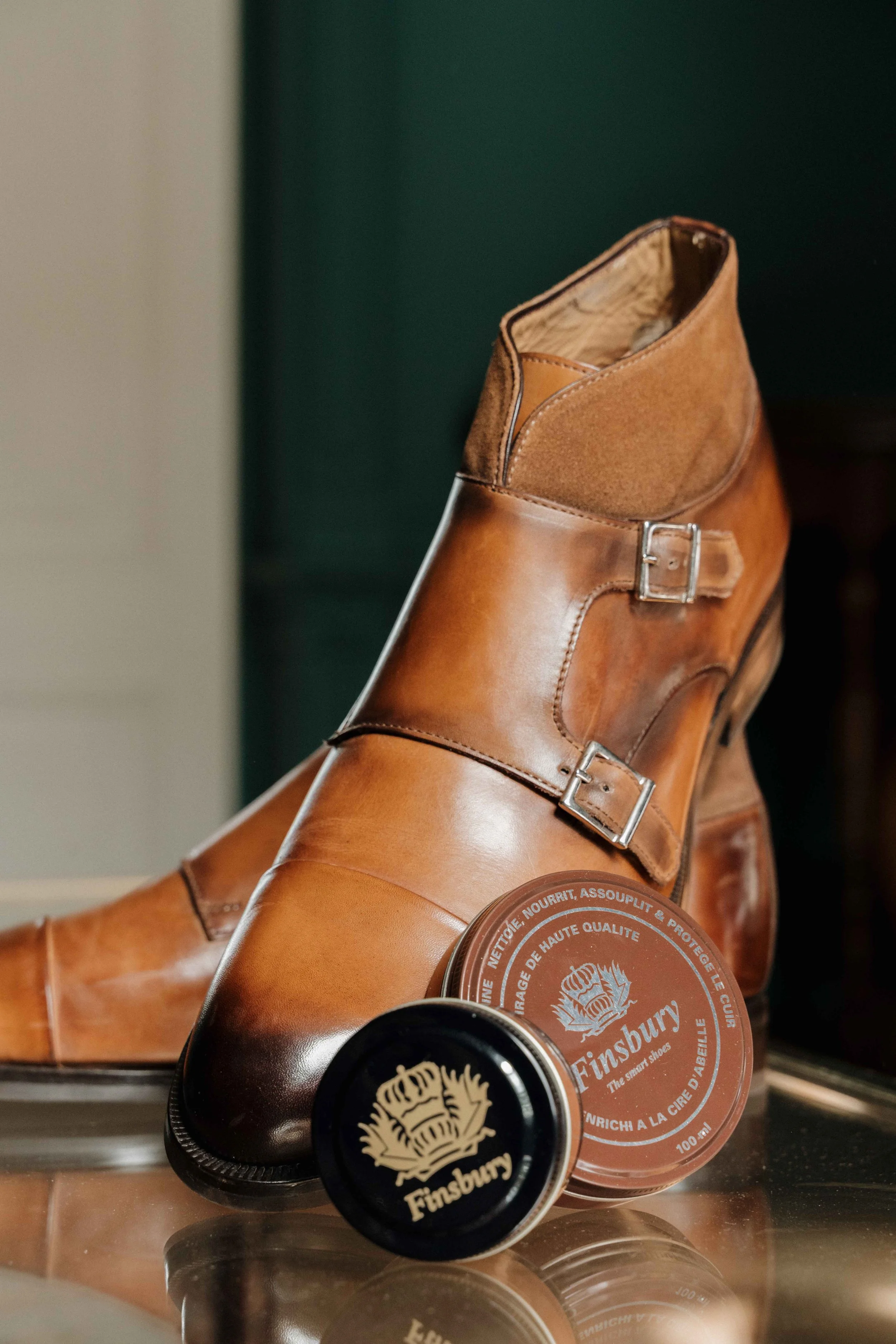 Une paire de chaussures en cuir marron avec des boucles, placée devant des pots de cirage de la marque Finsbury. Domaine de tourieux à Savigny dans le beaujolais à Lyon. Mariage cérémonie laïque, photographe Lyon haut de gamme, duo photographe