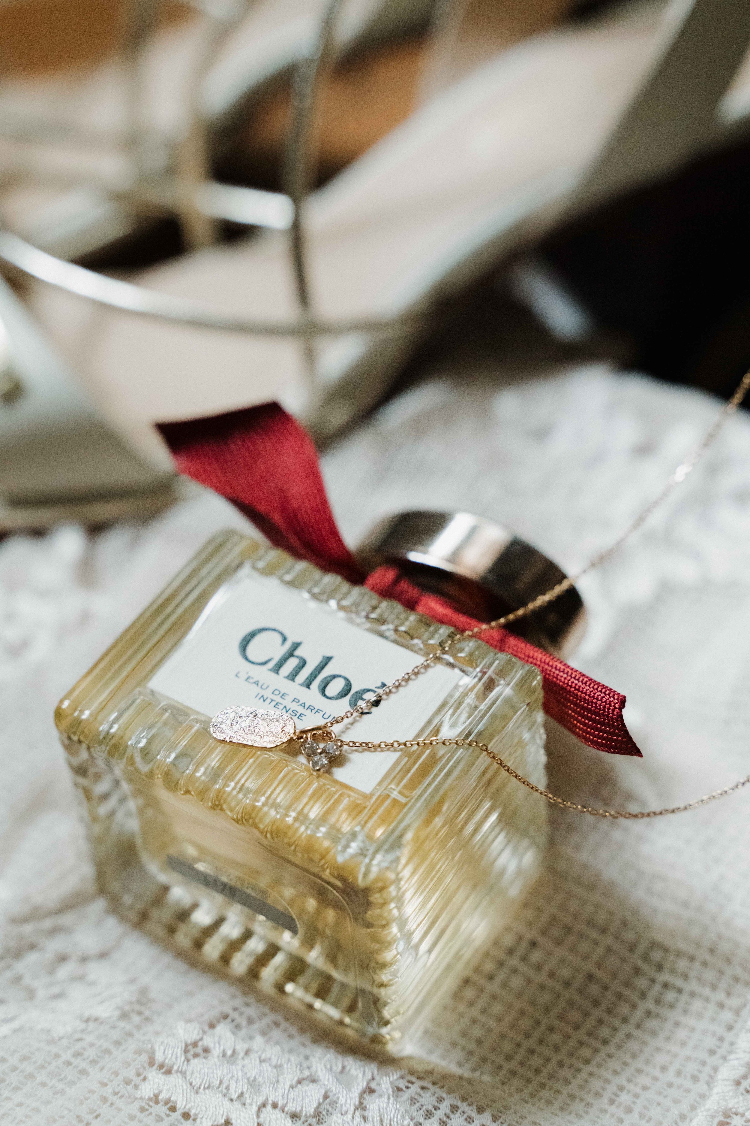 Flacon de parfum Chloe, collier en or avec pendentif en forme de cœur, bijoux reposant sur un linge blanc, fond avec boîte à bijoux et accessoires décoratifs. Domaine de tourieux à Savigny dans le beaujolais à Lyon. Mariage cérémonie laïque