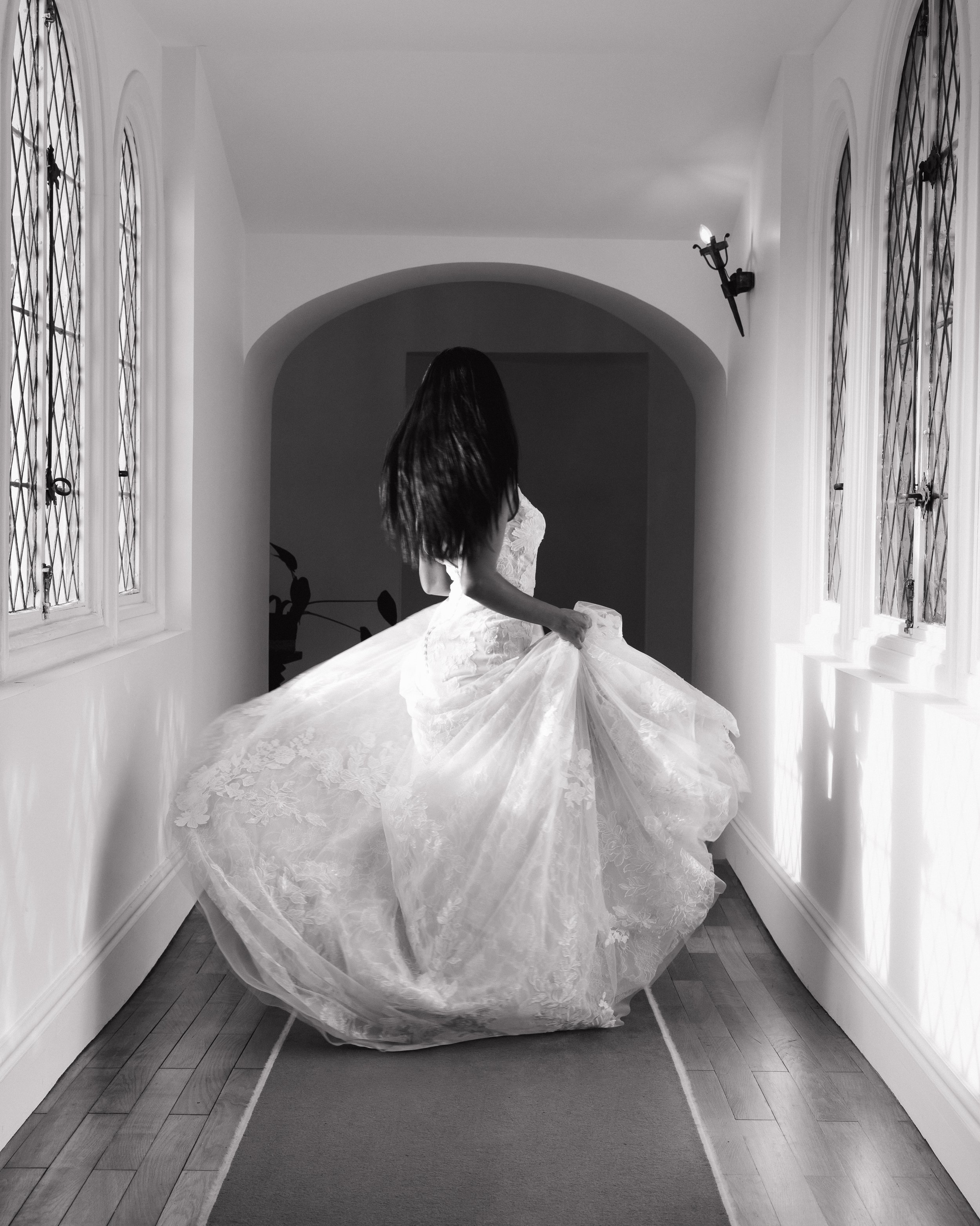 Une femme en robe de mariage qui tourne dans un couloir avec des fenêtres à vitraux.  session femme mariées et robes haut de gamme, brindos, hôtel et lac,  photographe mariage bordeaux et Lyon et destination wedding