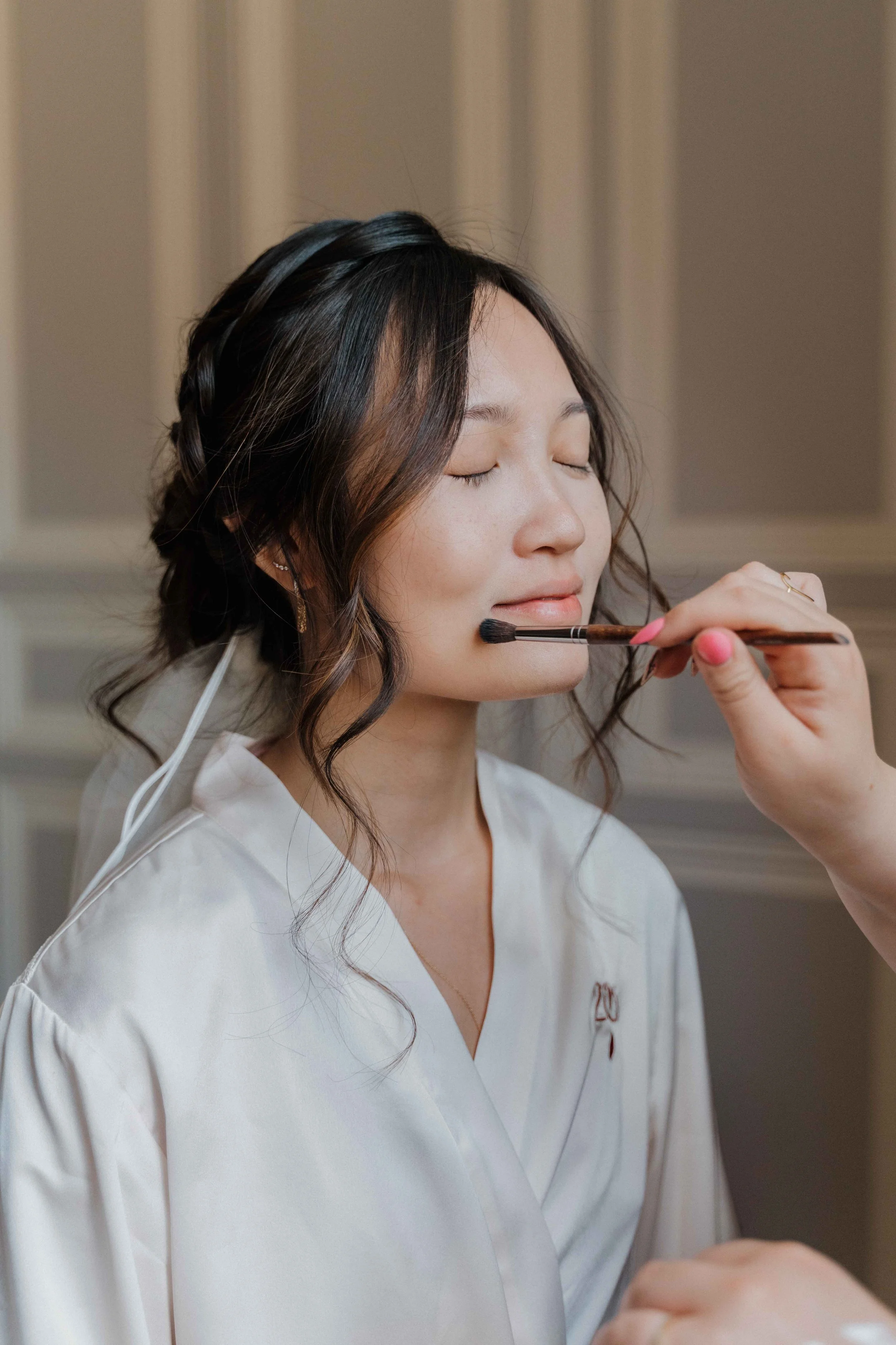 Une femme qui se fait maquiller, avec les yeux fermés et un léger sourire, portant une robe blanche. Domaine de tourieux à Savigny dans le beaujolais à Lyon. Mariage cérémonie laïque, photographe Lyon haut de gamme, duo photographe, argentique.