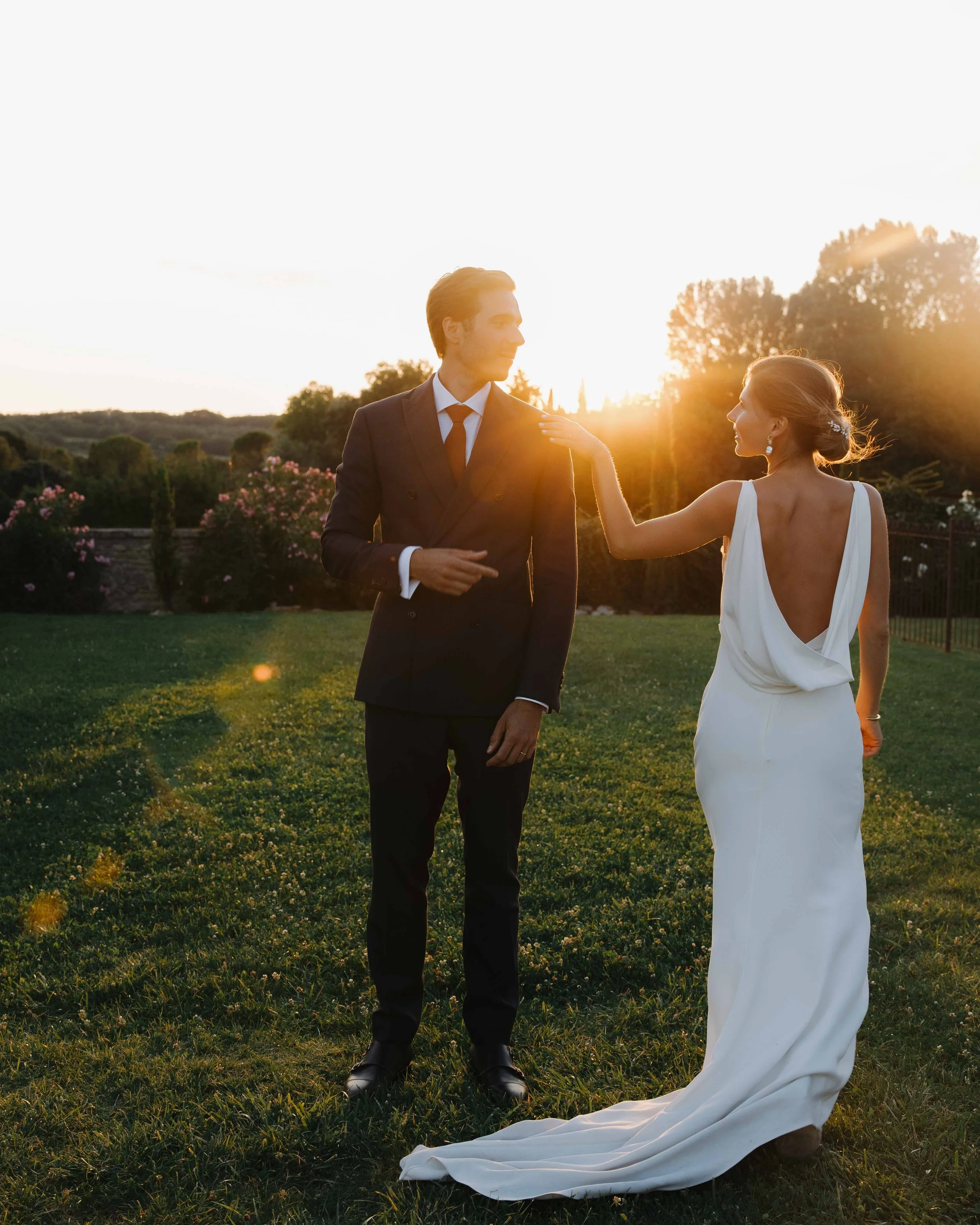 Un couple en robe de mariage et costume se tenant dans un jardin lors d'un coucher de soleil. Domaine du bijoutier à grignan, drome provençal, coucher de soleil, session couple, mariage religieux, cérémonie laïque, photographe mariage sud 