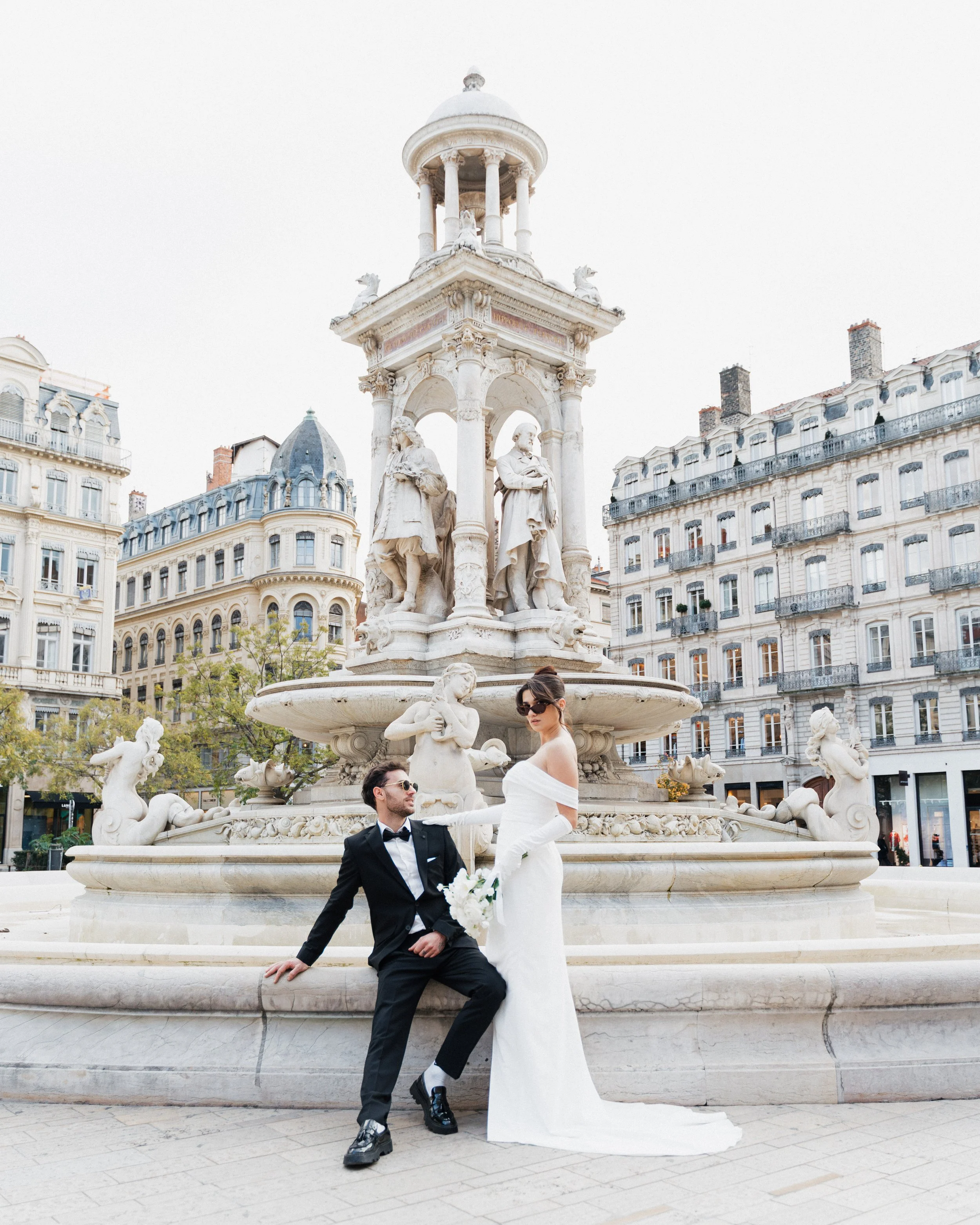 Un couple en session engagement posant devant une fontaine ornée de sculptures à Lyon place des jacobins, photographe duo haut de gamme mariage Lyon et bordeaux