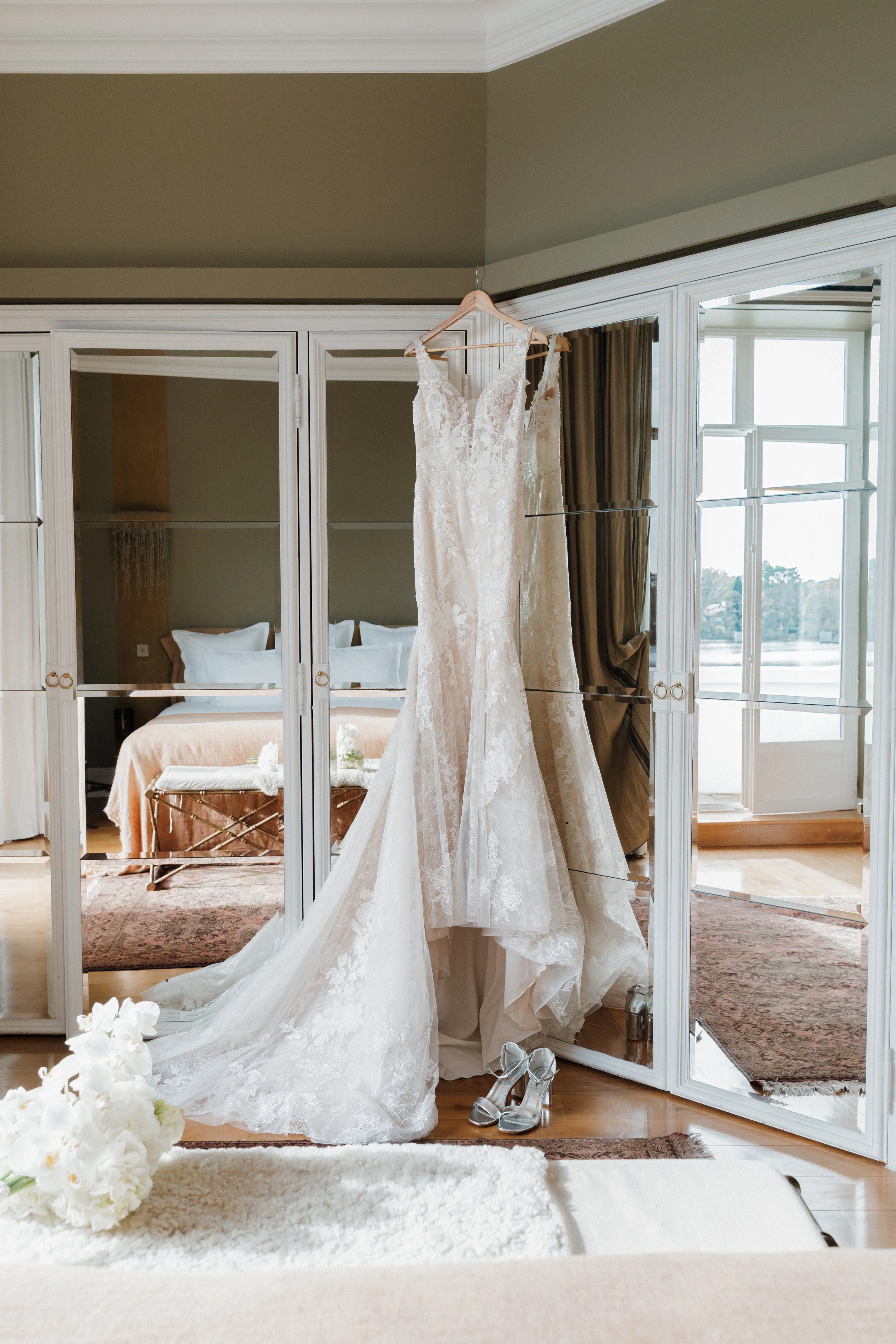 Robe de mariée blanche en dentelle suspendue devant un miroir dans une chambre lumineuse session femme mariées et robes haut de gamme, brindos, hôtel et lac,  photographe mariage bordeaux et Lyon et destination wedding