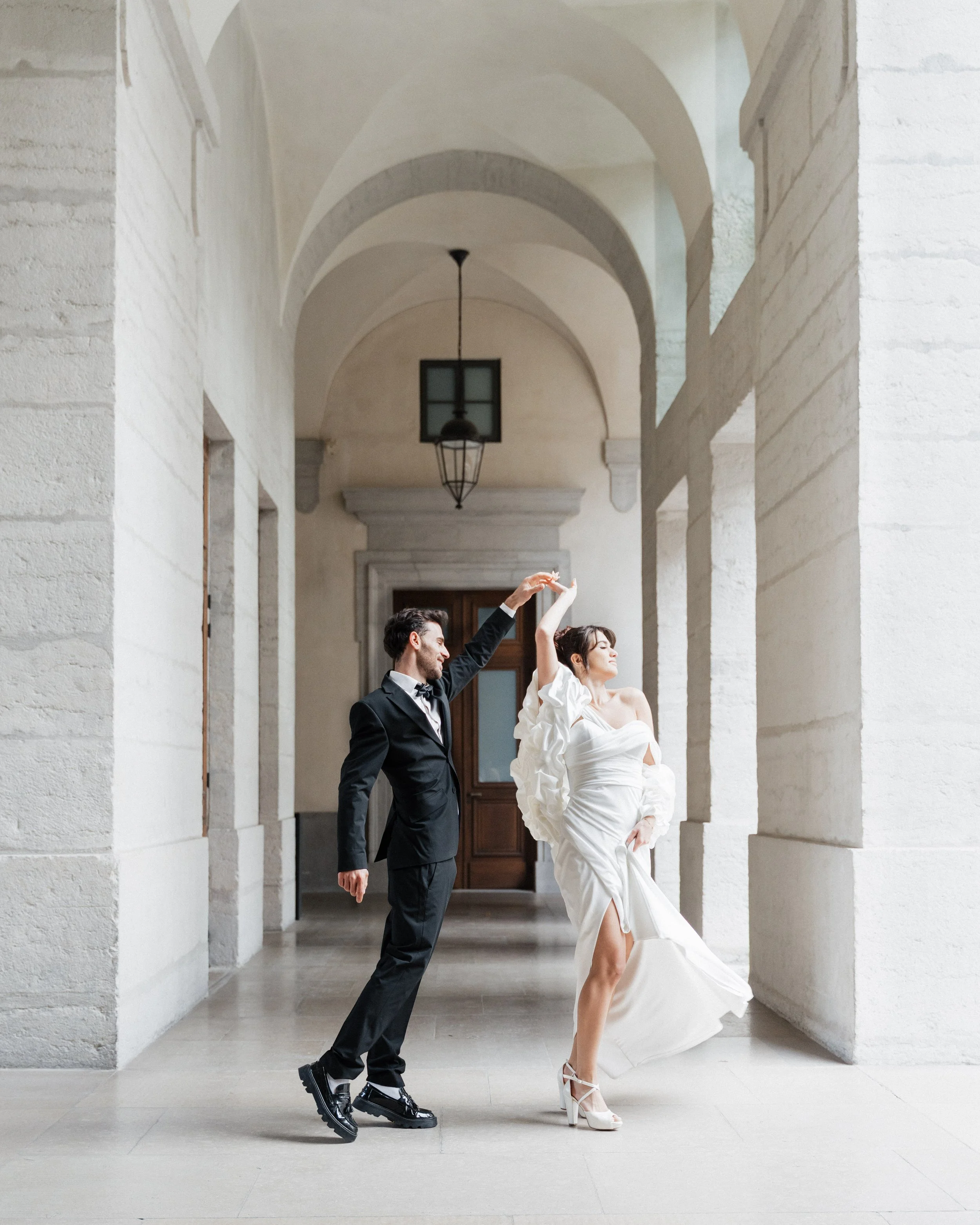 Un couple en tenue de mariage danse dans une architecture en pierre blanche avec haut plafonds et arches à Lyon 2ème à l'hôtel dieu à l'intercontinental lors d'une session engagement par un duo de photographe de mariage et de sessions couples.