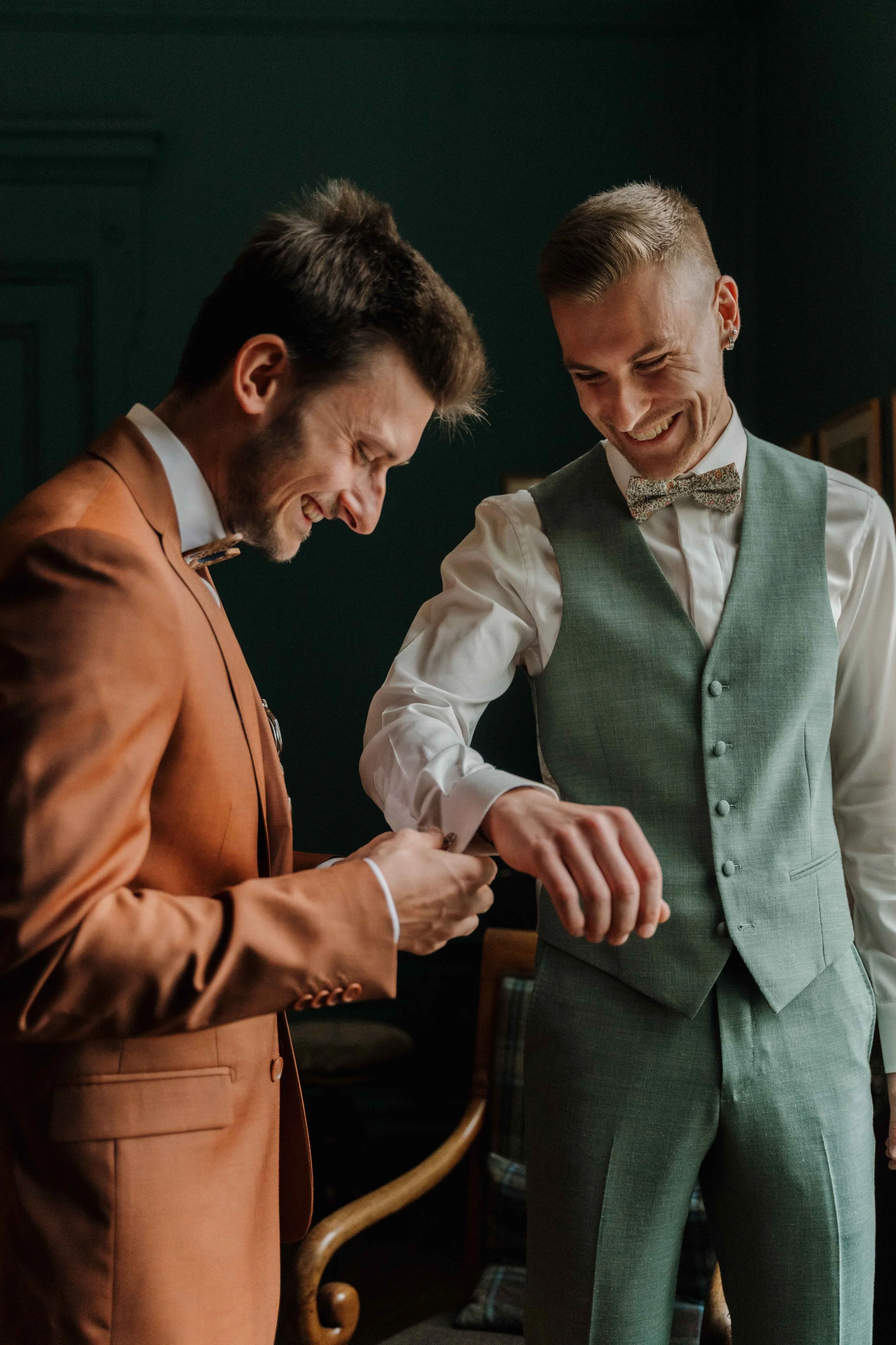 Deux hommes habillés en costumes élégants, souriant et riant, en train de rire ensemble dans une pièce élégante. Domaine de tourieux à Savigny dans le beaujolais à Lyon. Mariage cérémonie laïque, photographe Lyon haut de gamme, duo photographe
