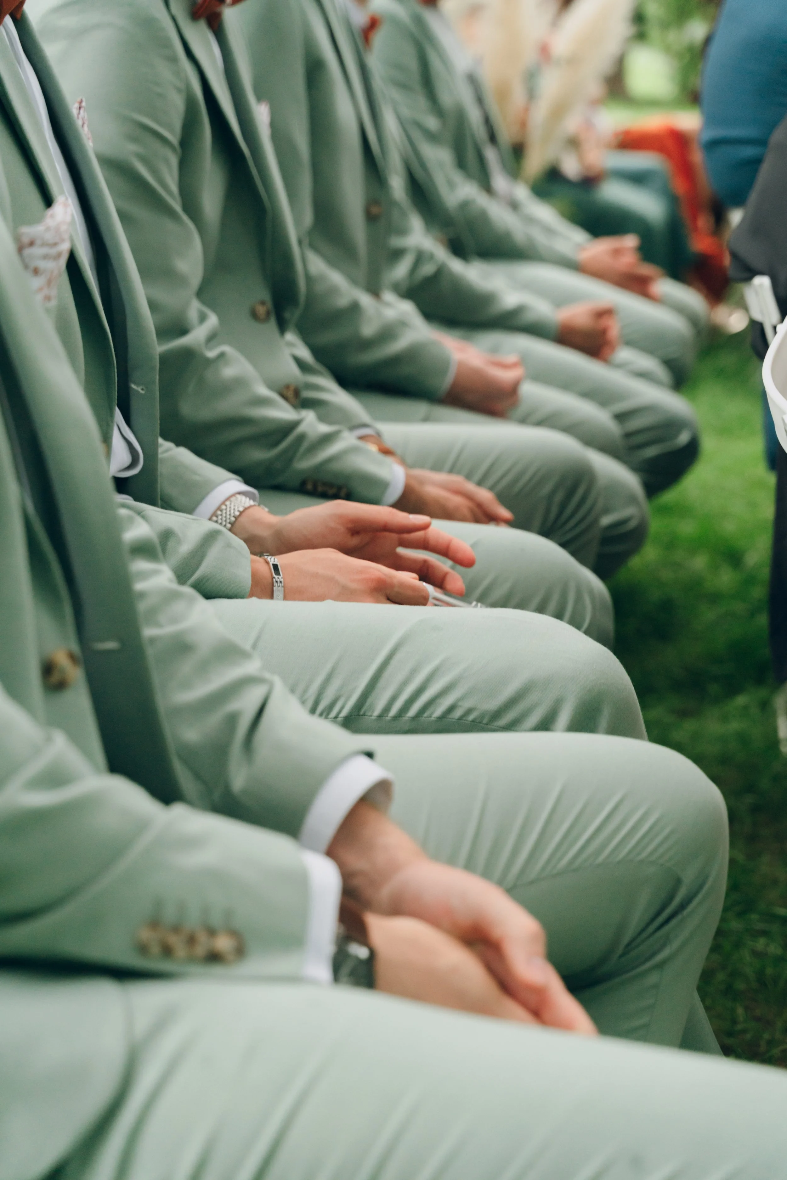 Groupe de personnes assises en rang lors d'une cérémonie, toutes portant des costumes en tissu satinée vert clair. Domaine de tourieux à Savigny dans le beaujolais à Lyon. Mariage cérémonie laïque, photographe Lyon haut de gamme, duo photographe 