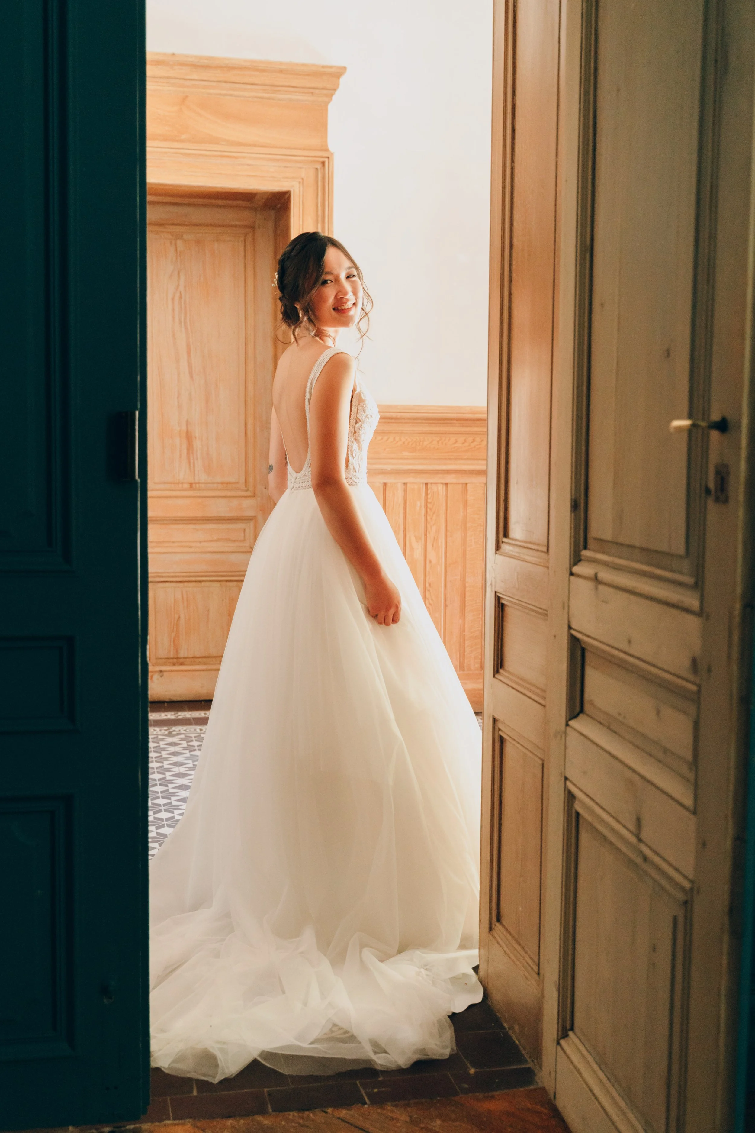 Jeune femme en robe de mariage blanche, souriante, dans une pièce avec murs en bois. Domaine de tourieux à Savigny dans le beaujolais à Lyon. Mariage cérémonie laïque, photographe Lyon haut de gamme, duo photographe, argentique.