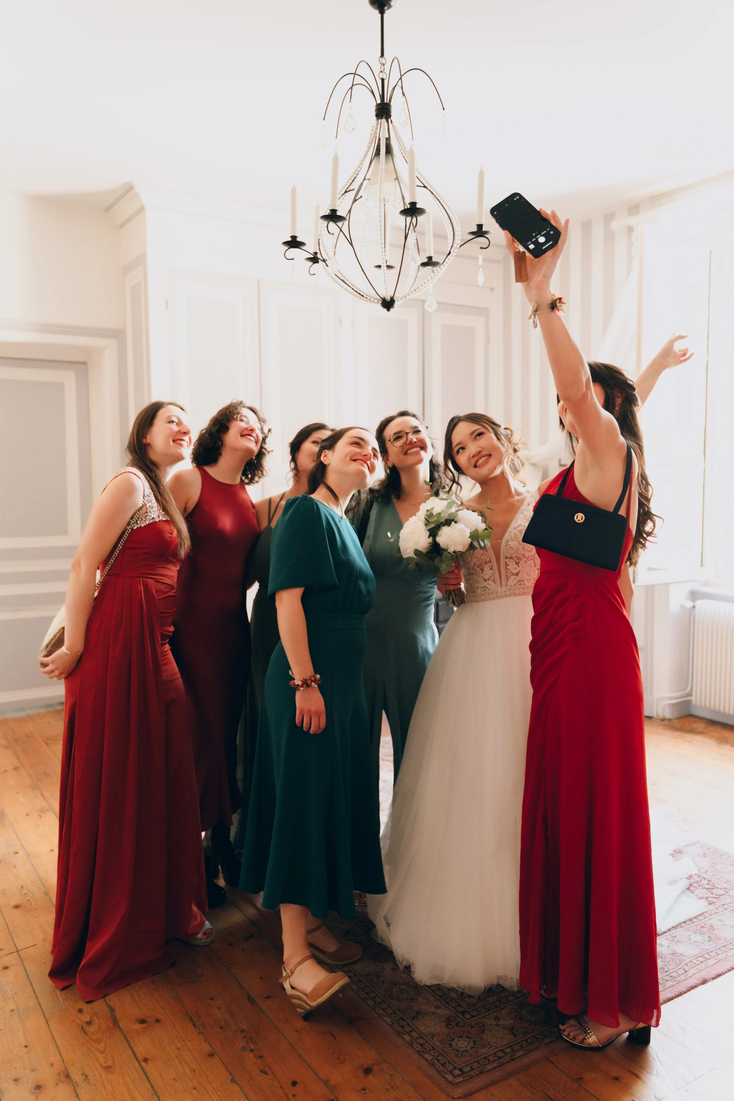 Un groupe de femmes souriantes prenant une photo lors d'une célébration, dont une femme en robe de mariée, dans une pièce bien éclairée. Domaine de tourieux à Savigny dans le beaujolais à Lyon. Mariage cérémonie laïque, photographe Lyon haut de gamme