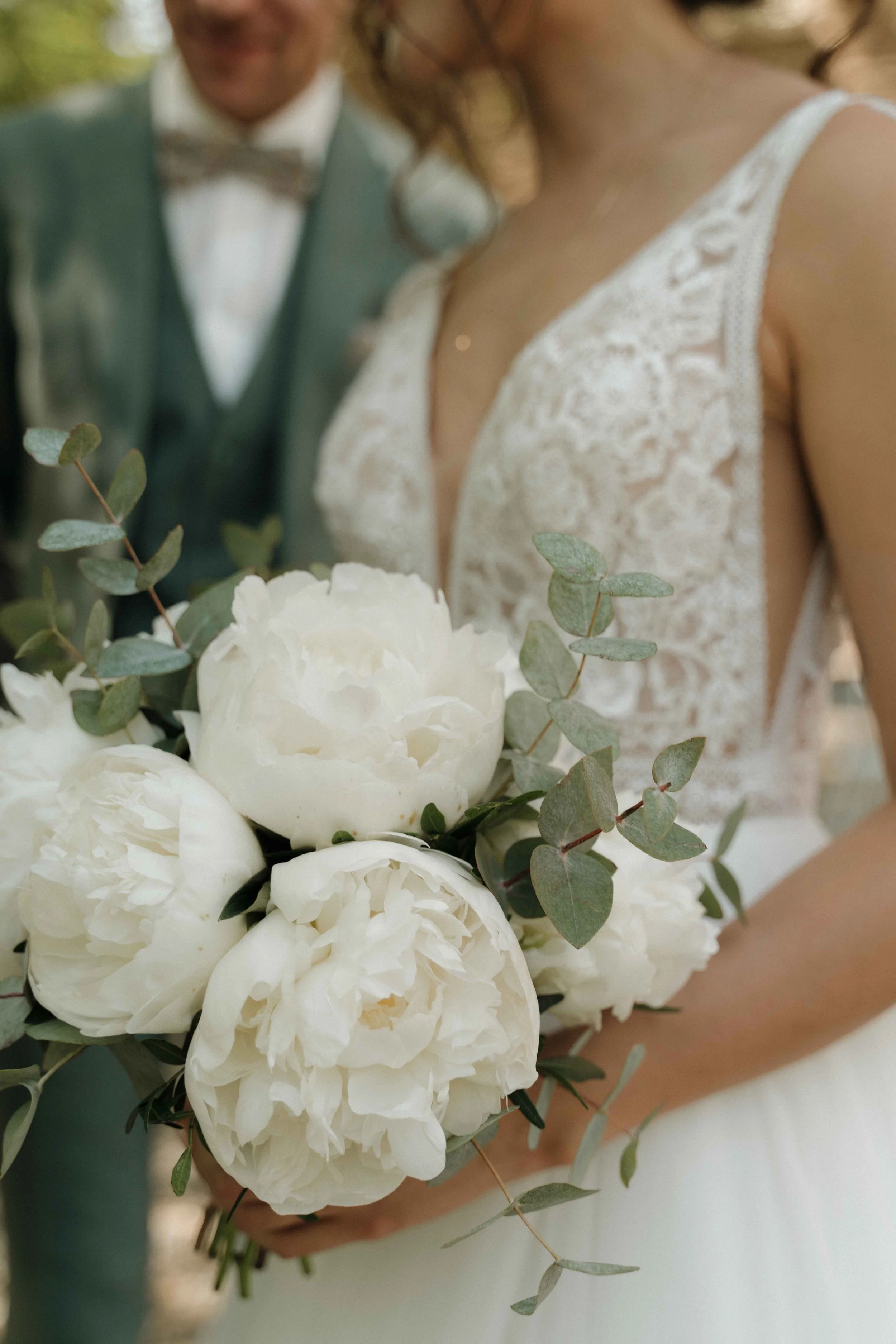 Un bouquet de fleurs blanches avec des feuilles de eucalyptus, tenu par une femme en robe de mariée lors d'un mariage. Domaine de tourieux à Savigny dans le beaujolais à Lyon. Mariage cérémonie laïque, photographe Lyon haut de gamme, duo photographe,