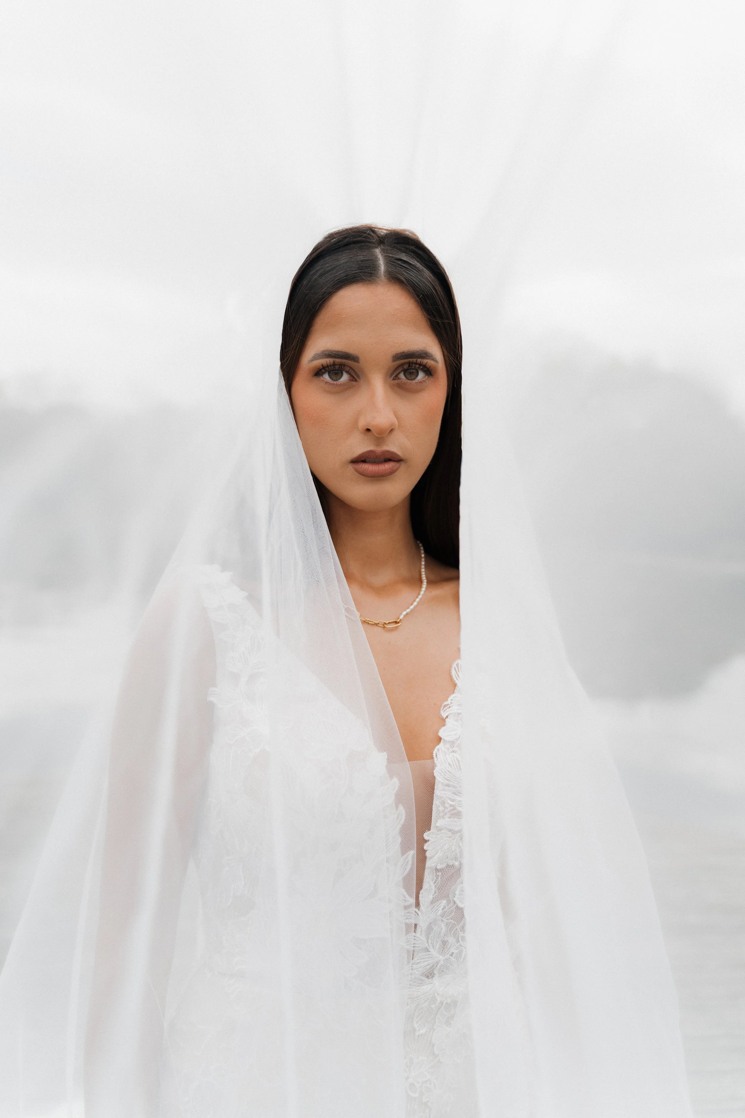 Femme portant un voile blanc, portrait en gros plan, fond flou, style élégant, ambiance neutre.  session femme mariées et robes haut de gamme, brindos, hôtel et lac,  photographe mariage bordeaux et Lyon et destination wedding