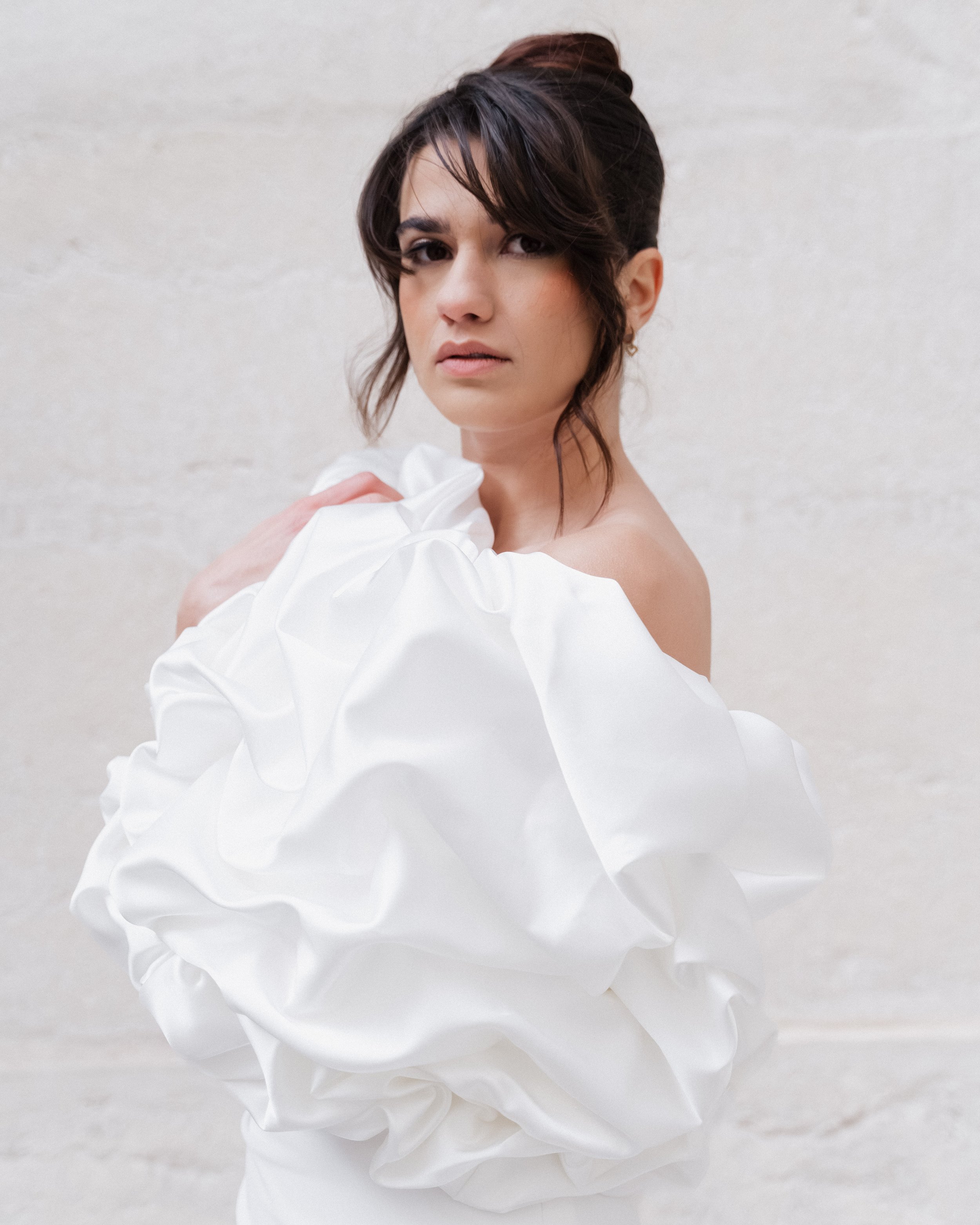 Une femme avec des cheveux bruns en hairstyle semi-attaché et vêtue d'une tenue blanche avec des manches bouffantes, regardant vers l'objectif, contre un fond neutre  à l'hôtel dieu à Lyon 2ème, à l'intercontinental, session engament, photographe