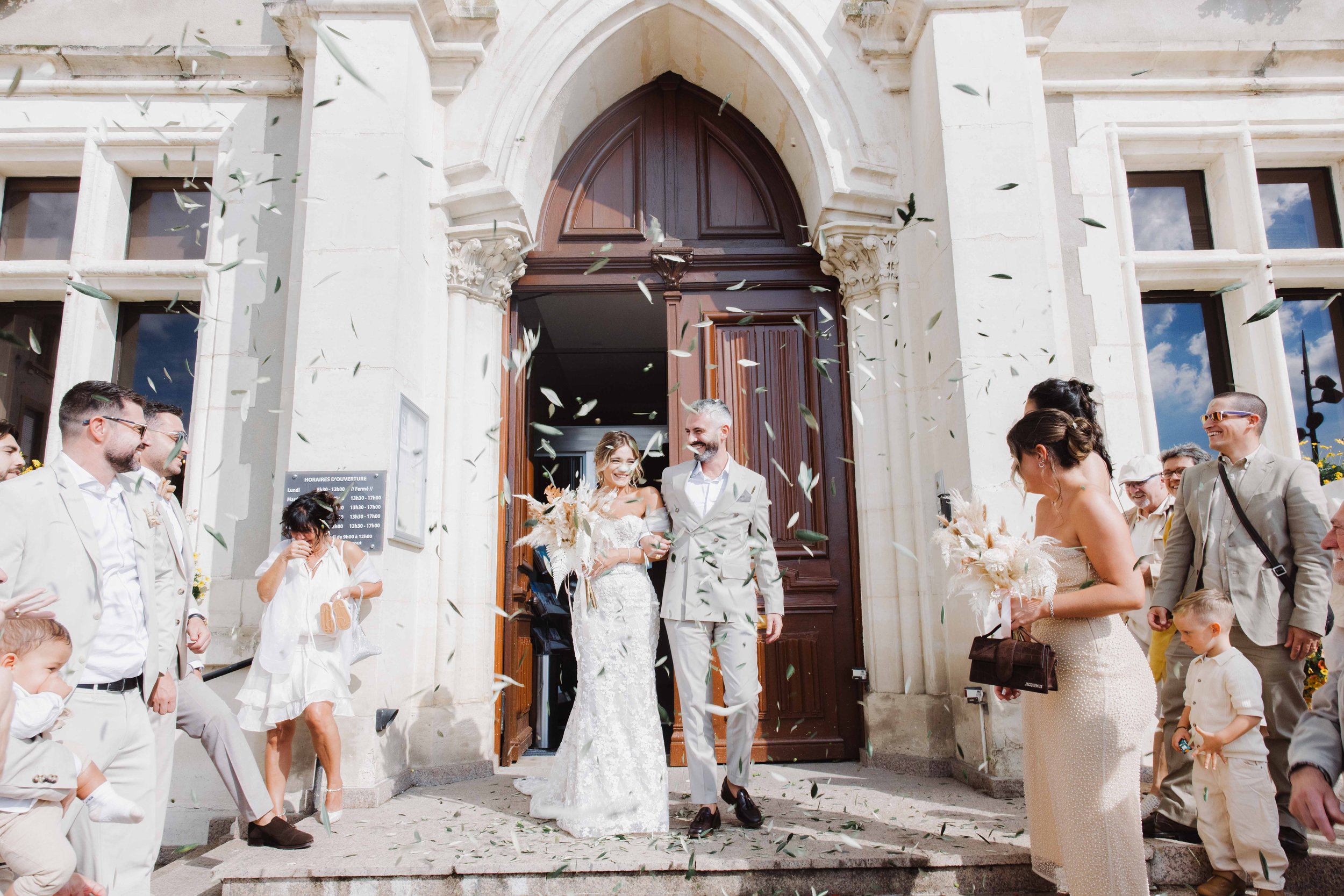 Un couple de mariés sortant de l'église sous une pluie de fleurs, entouré de leurs invités lors d'un mariage en plein air. Photographe mariage Isère, ferme du rocher, cérémonie civil et laïque. Bordeaux et Lyon et destination wedding.