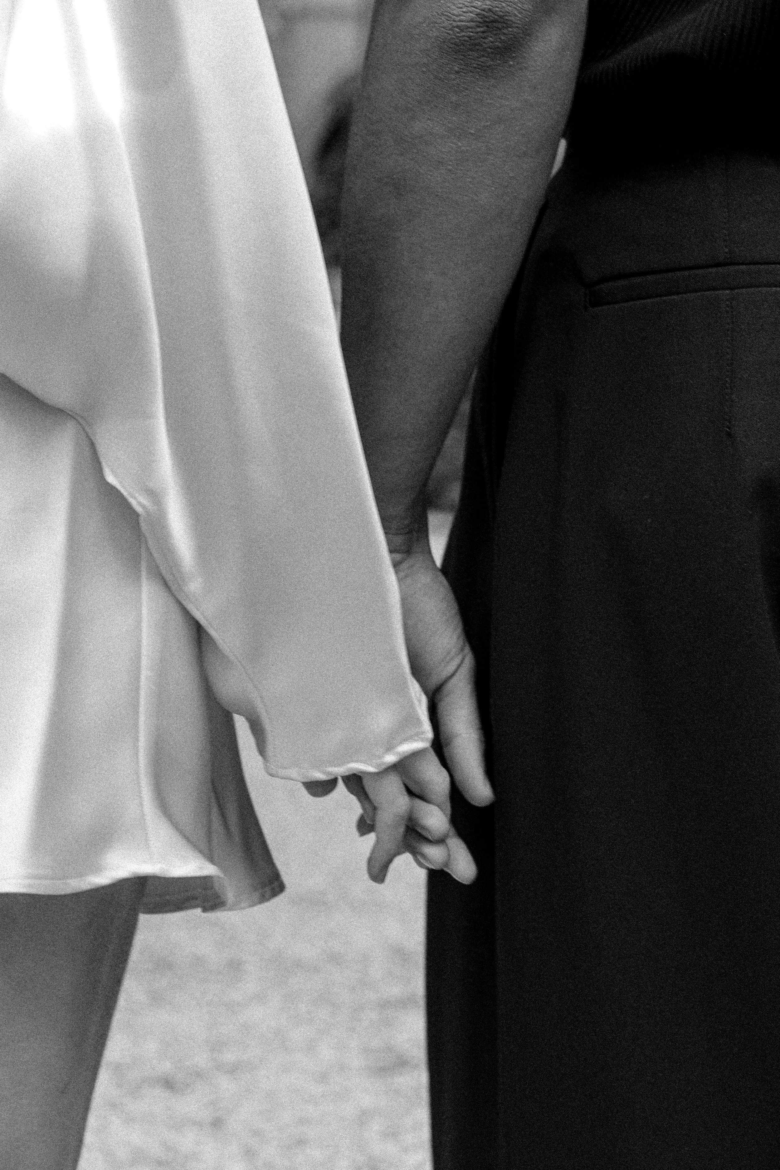 Une paire de mains croisées, une homme et une femme, tenu par la main dans un contexte apparemment formel ou cérémonial à l'hôtel dieu à Lyon 2ème, à l'intercontinental, session engament, photographe mariage duo haut de gamme.