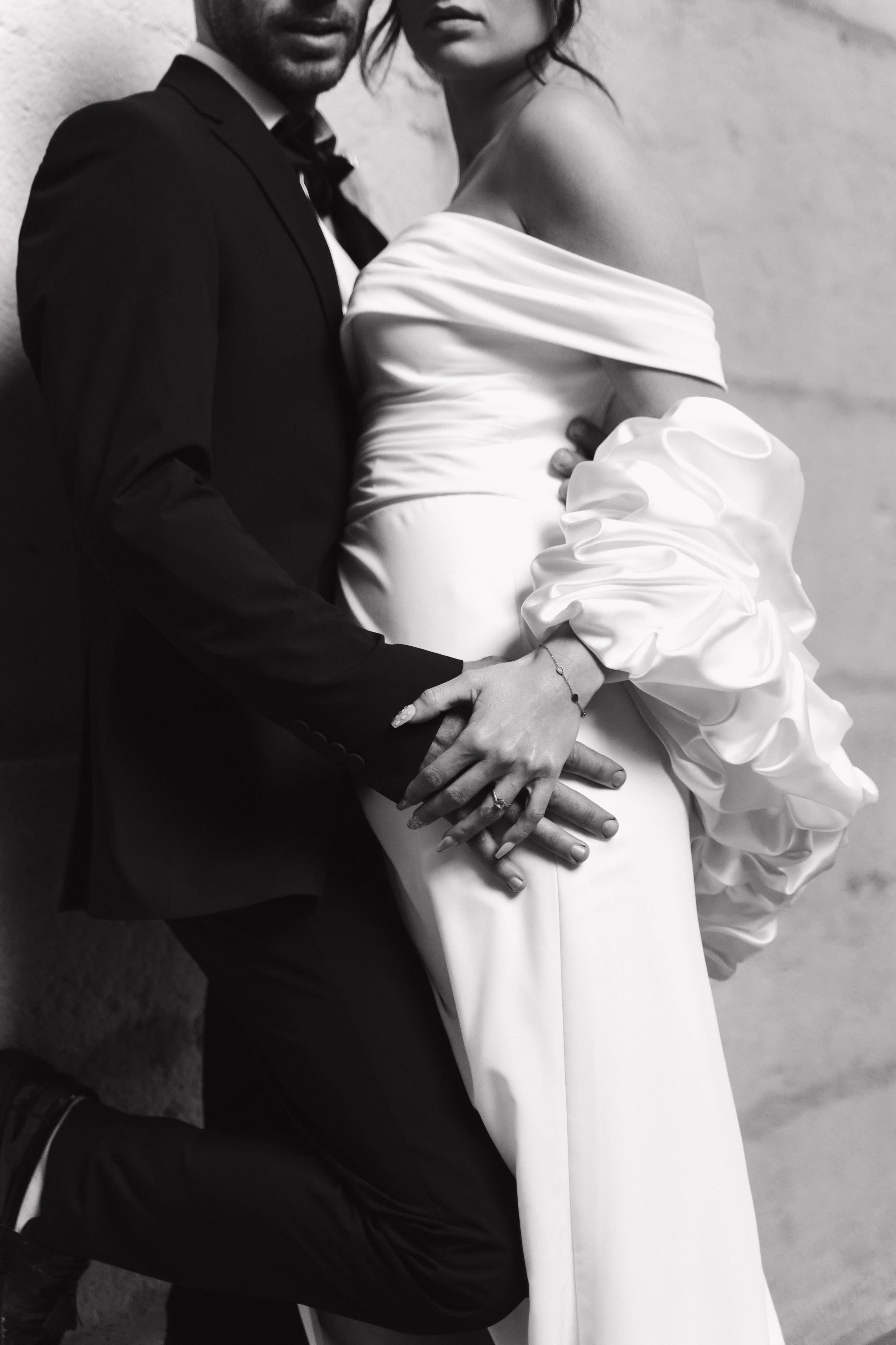 Une photo en noir et blanc d'un couple en tenue de mariage, la femme portant une robe blanche avec des détails bouffants et le homme en costume noir, en position proche, avec leurs mains entremêlées à Lyon 2ème à l'hôtel dieu à l'intercontinental.