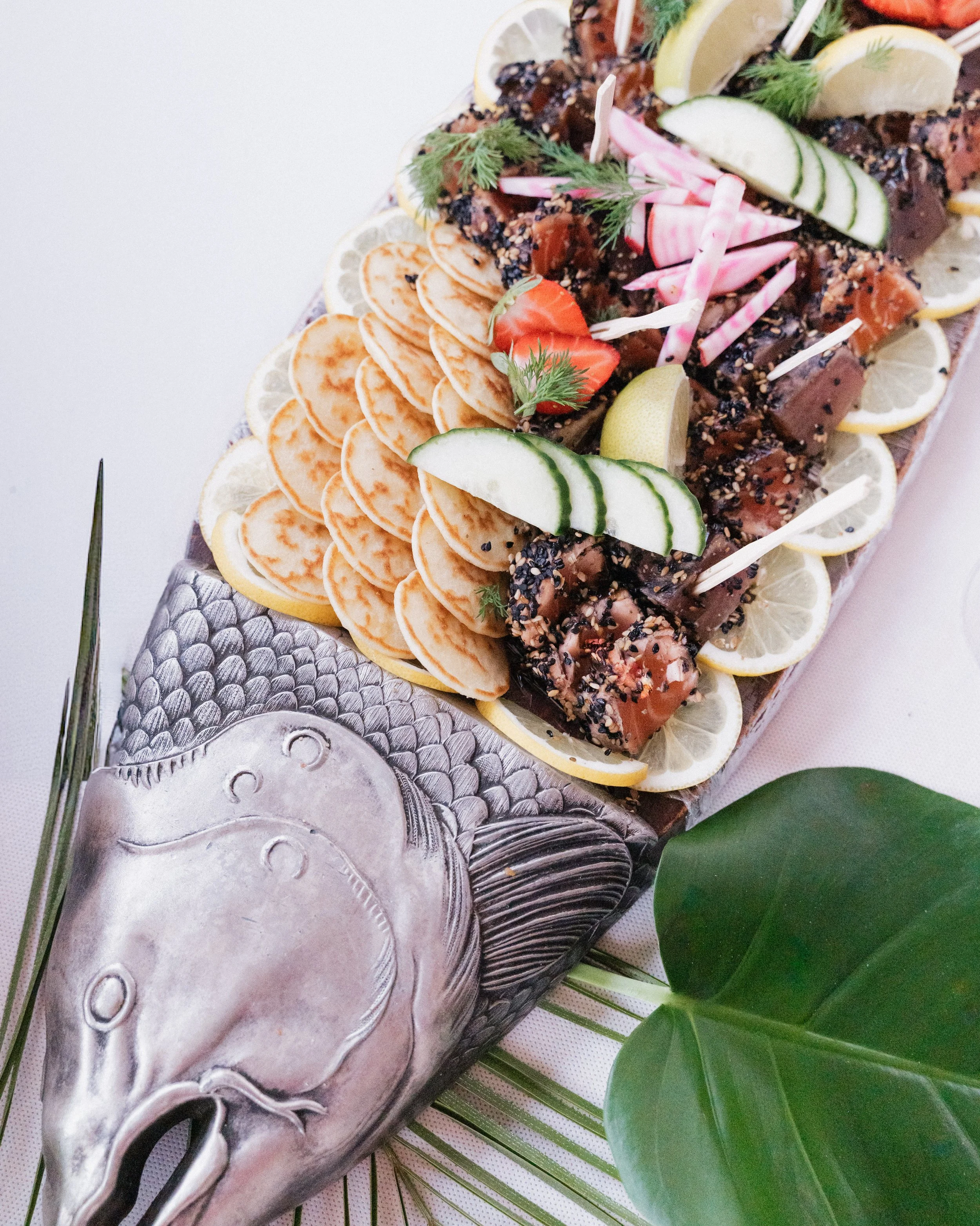 Plate de poisson cru avec citron, concombre, radis, et herbes, décorée de tranches de citron et de concombre, servie sur un plateau en forme de poisson, avec des feuilles vertes autour. Domaine de tourieux à Savigny dans le beaujolais à Lyon. 