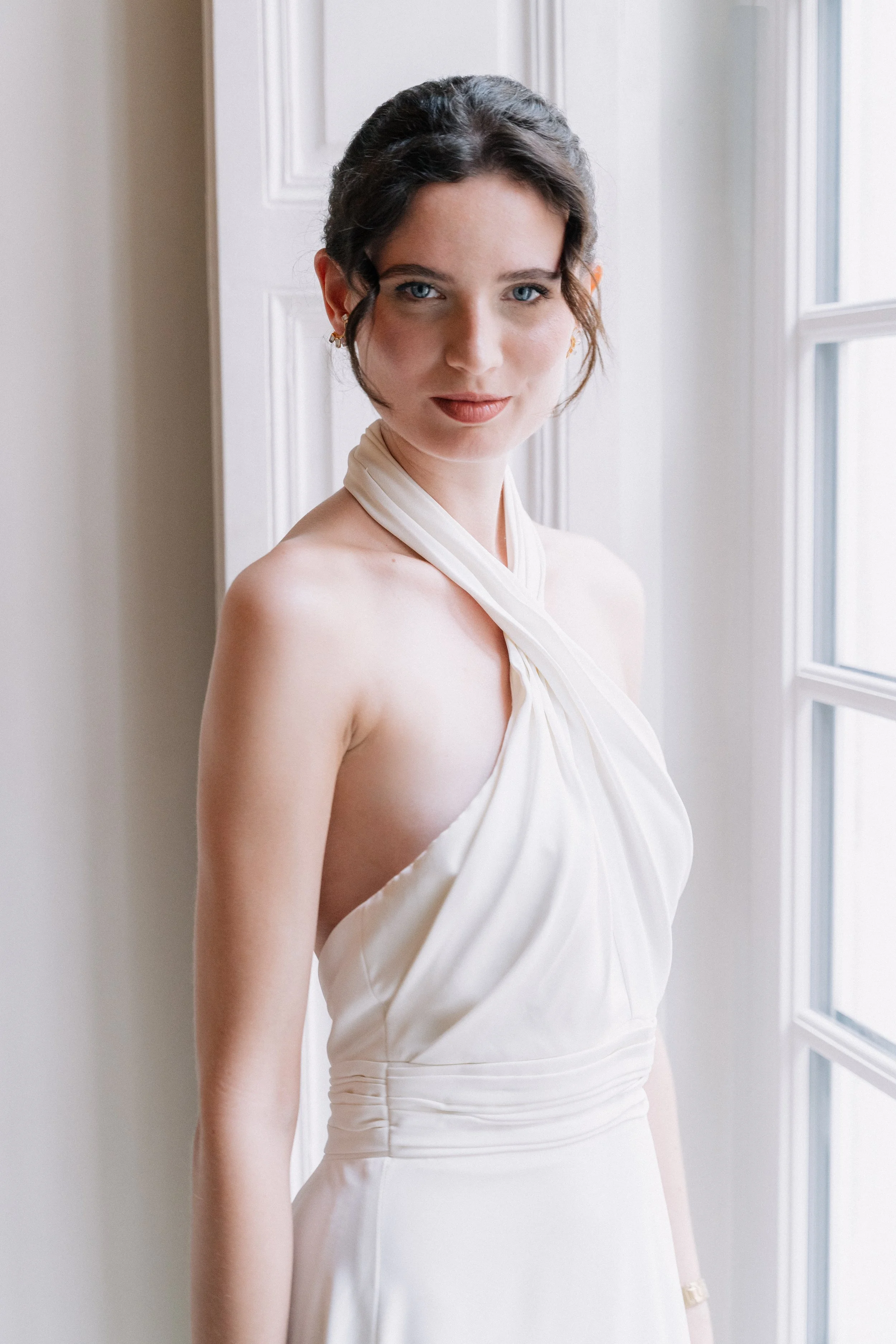 Jeune femme portant une robe blanche élégante, posant près d'une fenêtre avec une lumière douce. Session engagement paris, Louvre, mariage haut de gamme, destination wedding. Robe de mariées, madame a dit oui