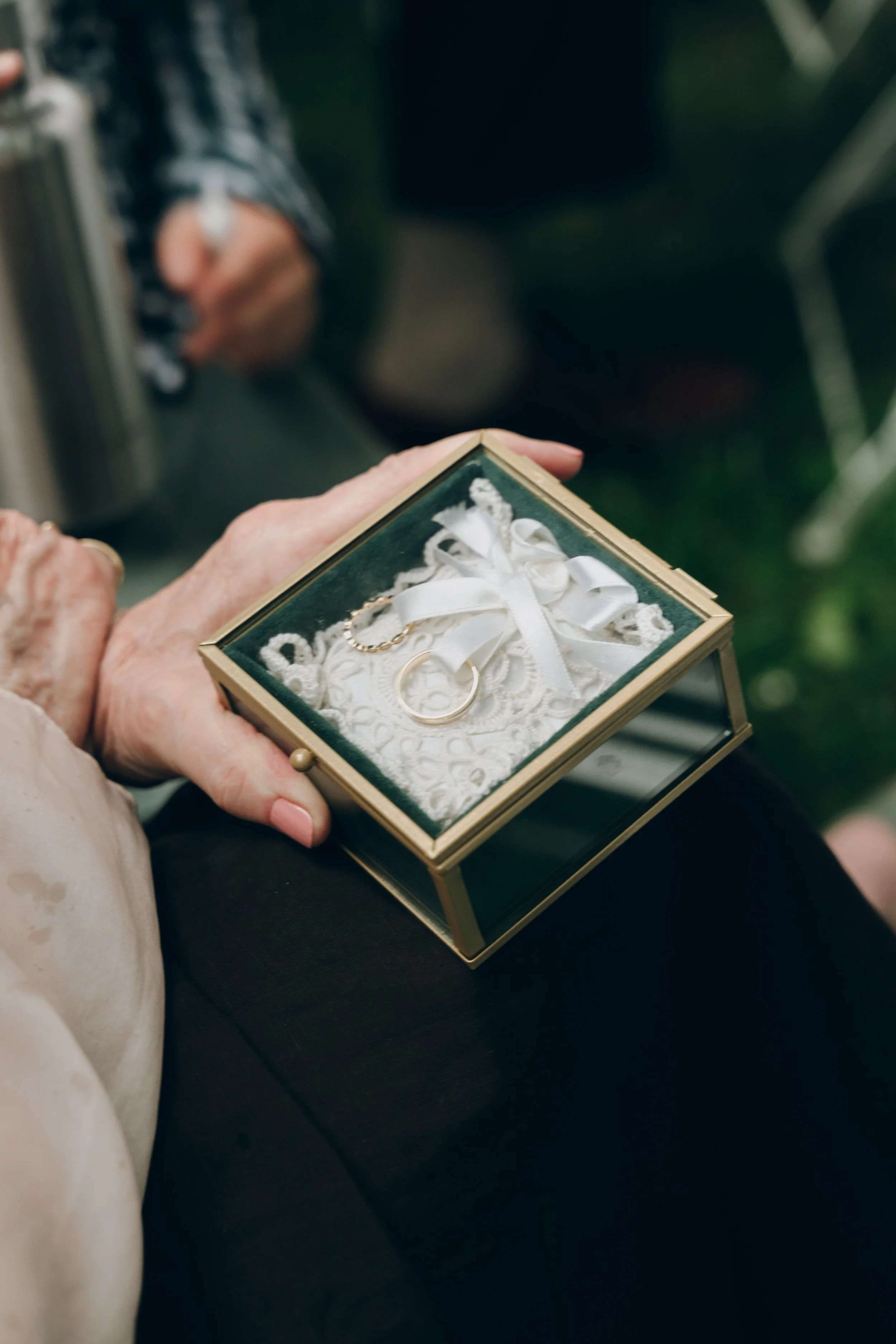 Une personne âgée tient une boîte en verre contenant une alliance de mariage, une chaîne en or et un nœud en satin blanc, probablement un souvenir de mariage. Domaine de tourieux à Savigny dans le beaujolais à Lyon. Mariage cérémonie laïque, film