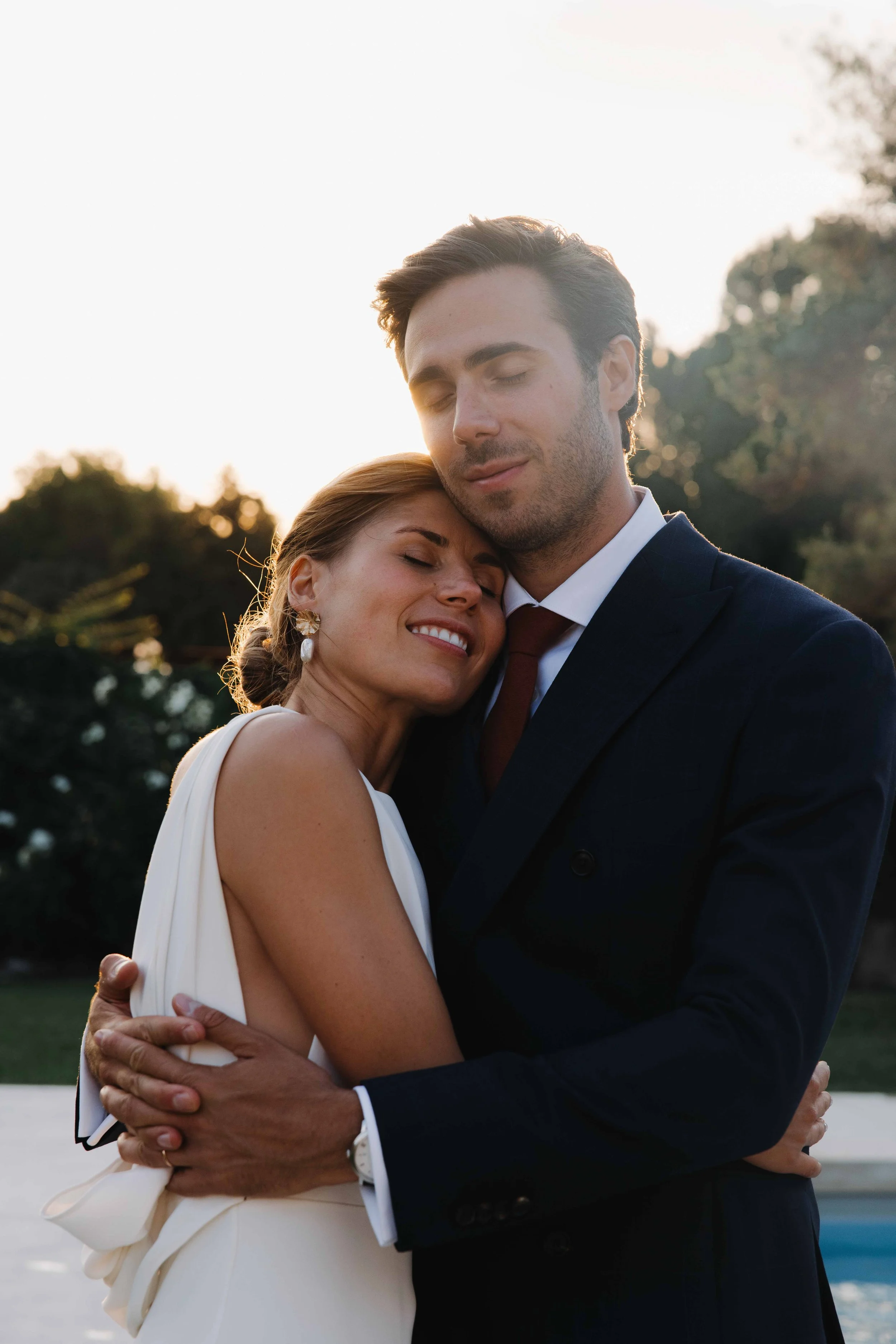 Un homme et une femme en costume d'affaires s'étreignent, yeux fermés, dans une ambiance chaleureuse. Domaine du bijoutier à grignan, drome provençal, coucher de soleil, session couple, mariage religieux, cérémonie laïque, photographe mariage sud 