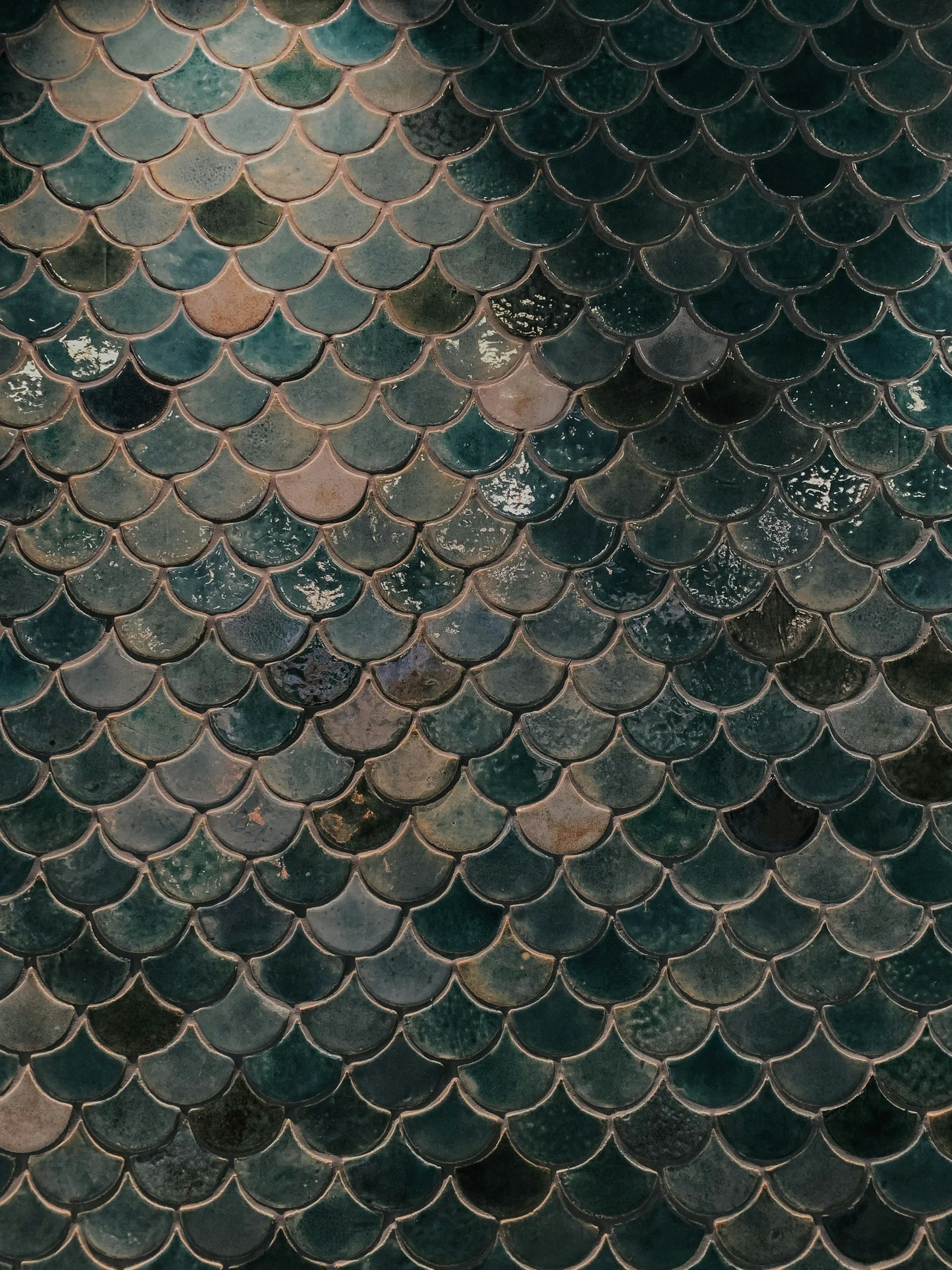 Close-up view of fish scale-style ceramic tiles with a glossy finish in various shades of blue and green.