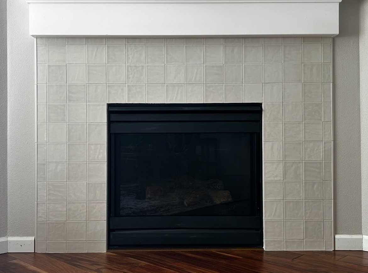 Fireplace enclosure with tinted glass surrounded by white handmade tiles from bedrosians with a white mantel in a living room with wooden floors. A very high end look.