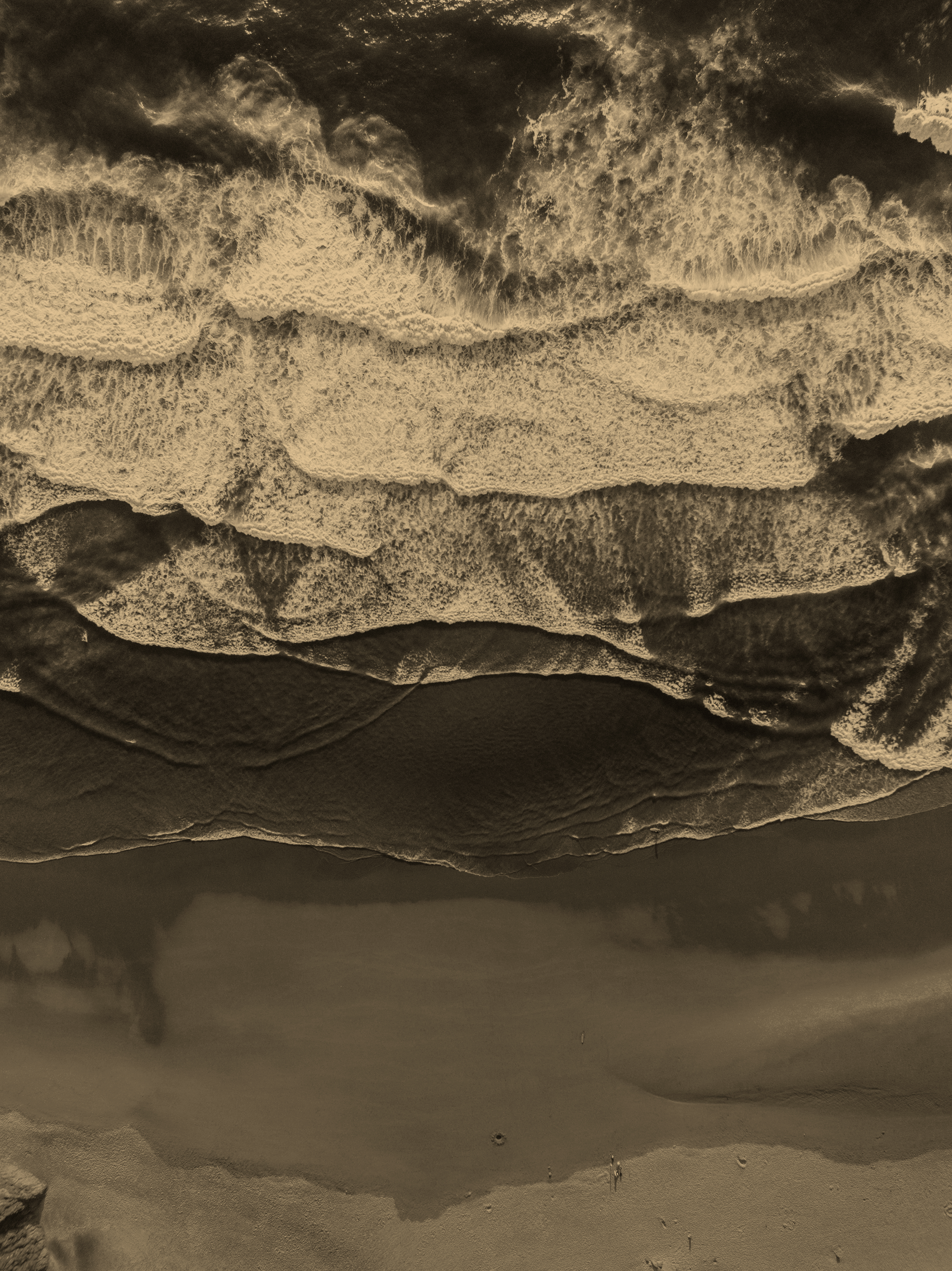 Upside down view of ocean waves crashing onto the beach with foam, sand in the foreground