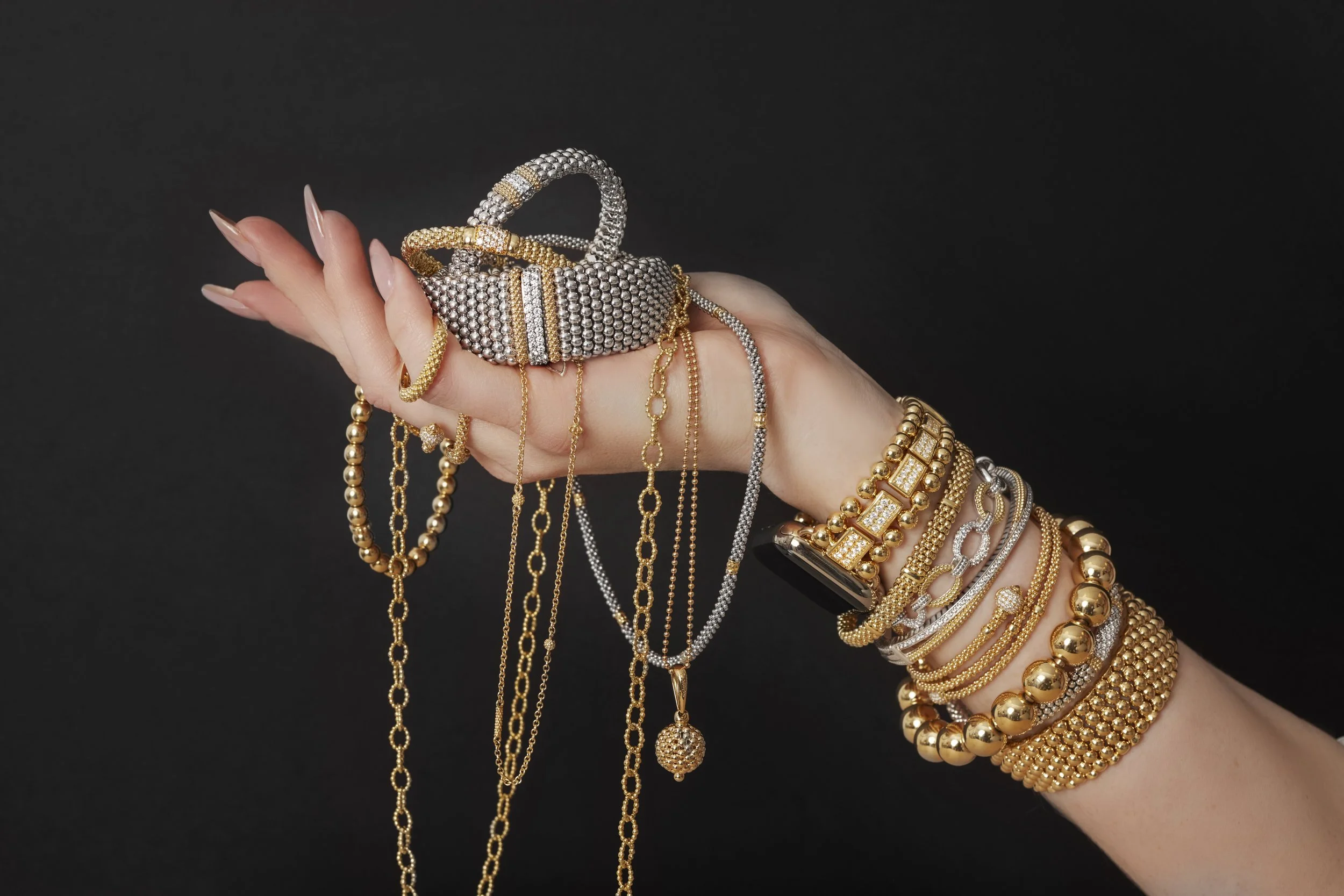 A hand wearing multiple gold and silver bracelets, with several gold and silver necklaces and rings, holding a collection of chunky jewelry.