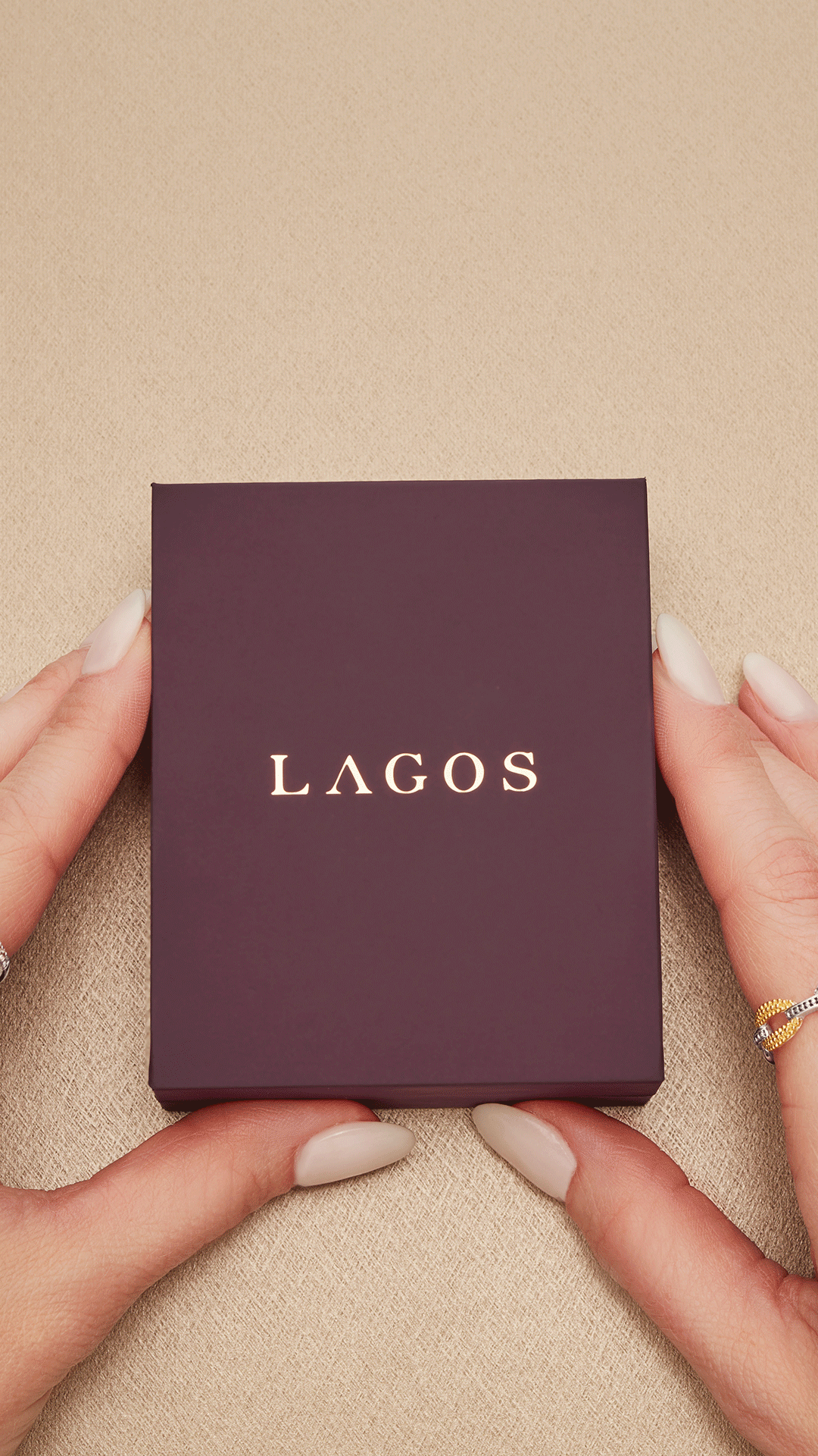 A hand holding a dark purple box with the word 'LAGOS' on it in white lettering, against a beige background.