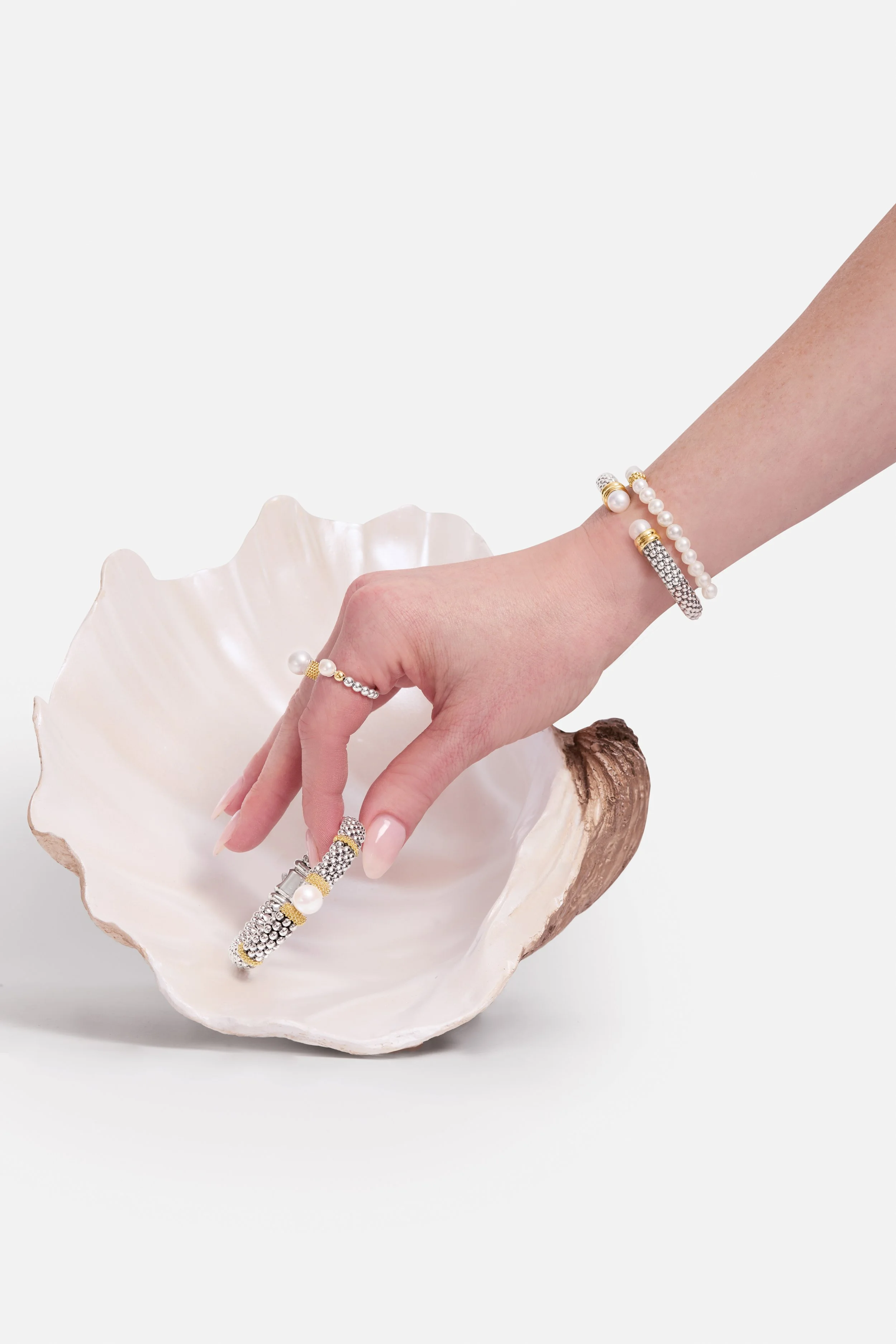 A hand displaying various jewelry pieces including rings, bracelets, and a ring with pearls and rhinestones, resting on a seashell-shaped dish.
