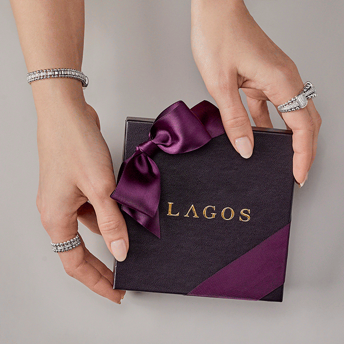 Two hands holding a black gift box with a purple ribbon and the word LAGOS in gold lettering, against a gray background.