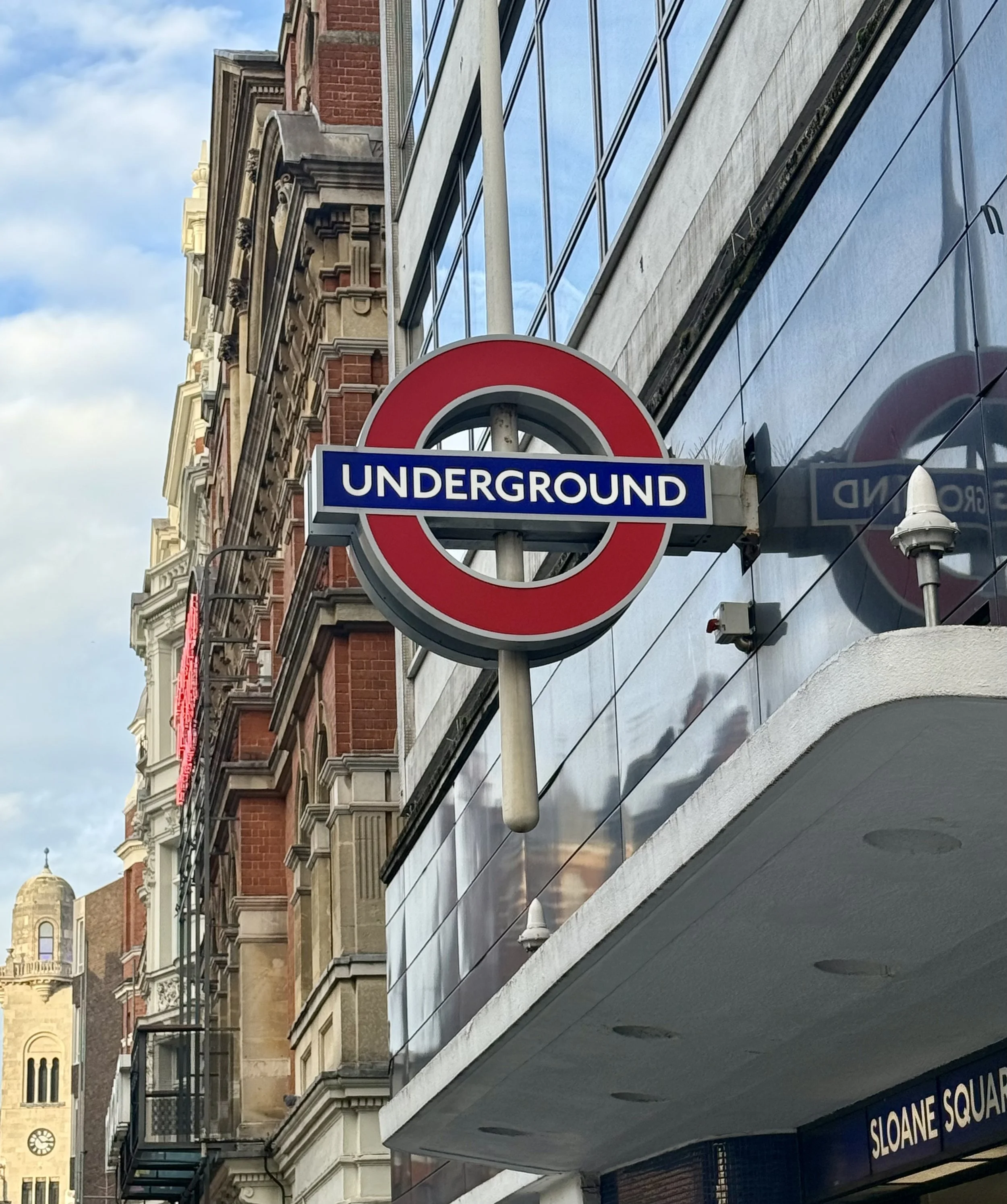 London Underground sign in front of a modern building on Sloane Square street.