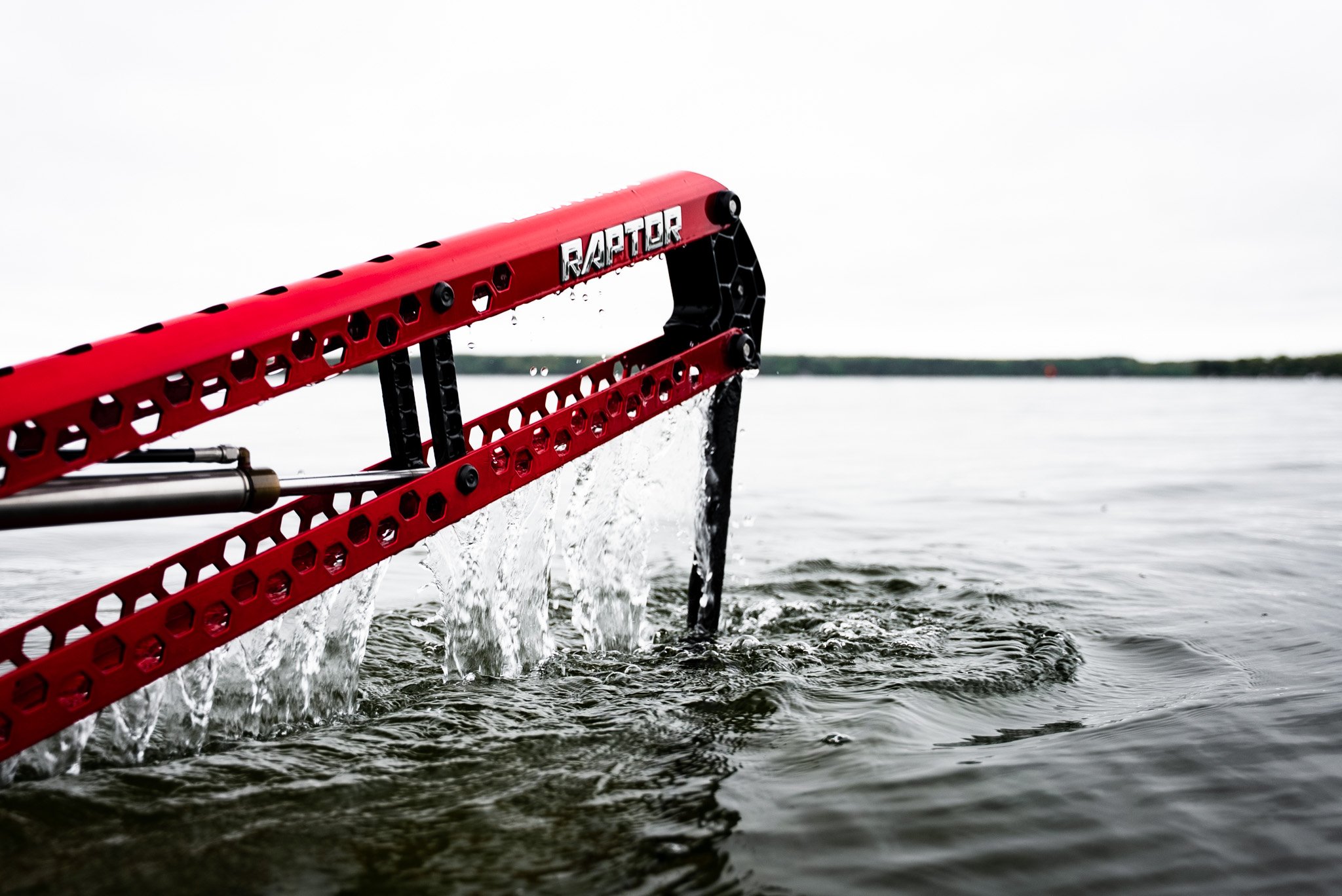 A red and black watercraft with the label 'Raptor' on it, partially submerged in water, with water spraying from its structure.