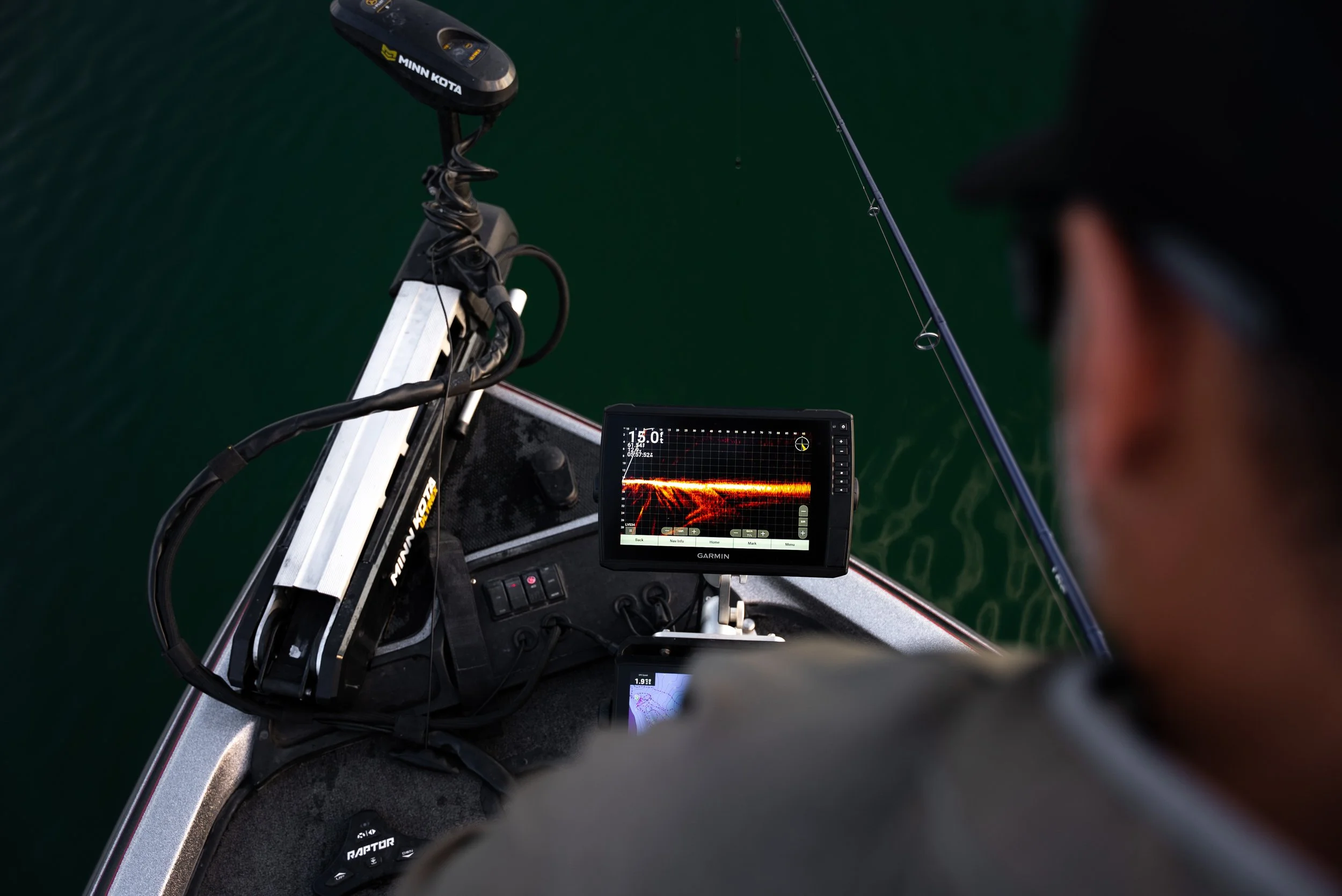 A person on a boat using a Garmin fishfinder with a sonar display showing fish activity beneath the water surface.