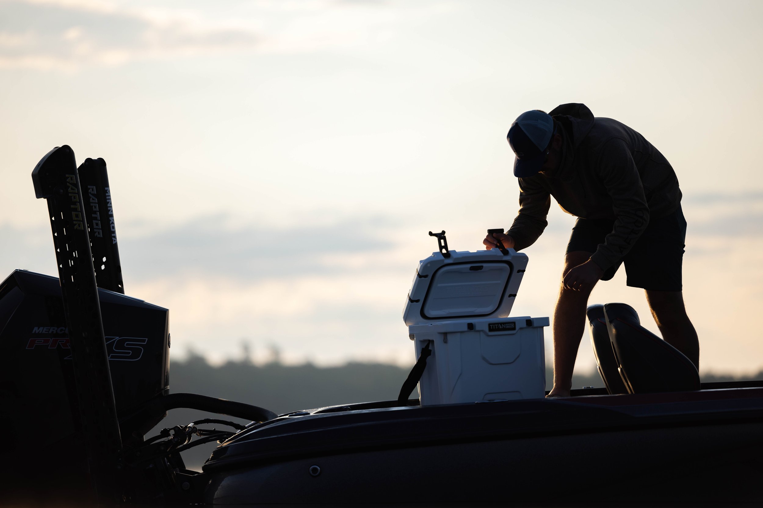 Person on a boat grabbing a cooler from the deck during sunset or sunrise.