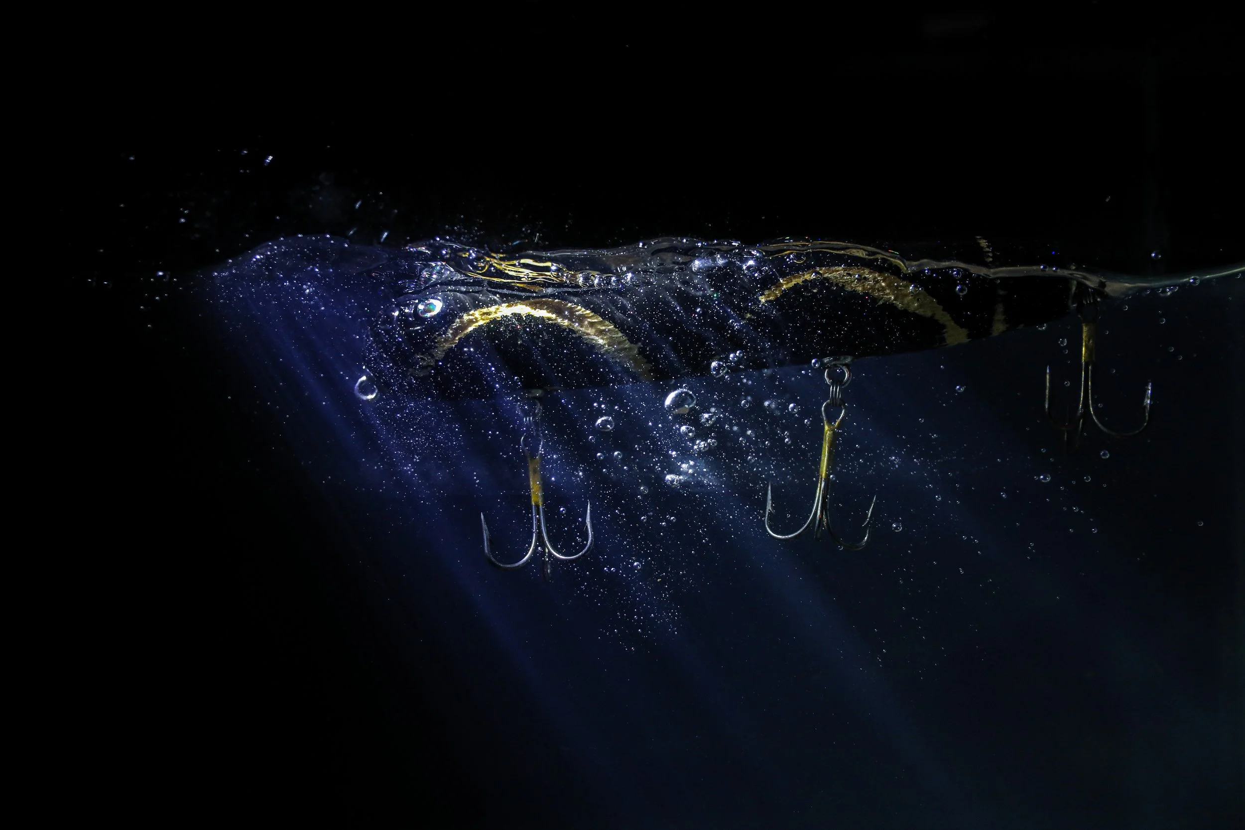 Underwater view of fishing lures hanging from a line, with bubbles and water movement visible in the dark background.