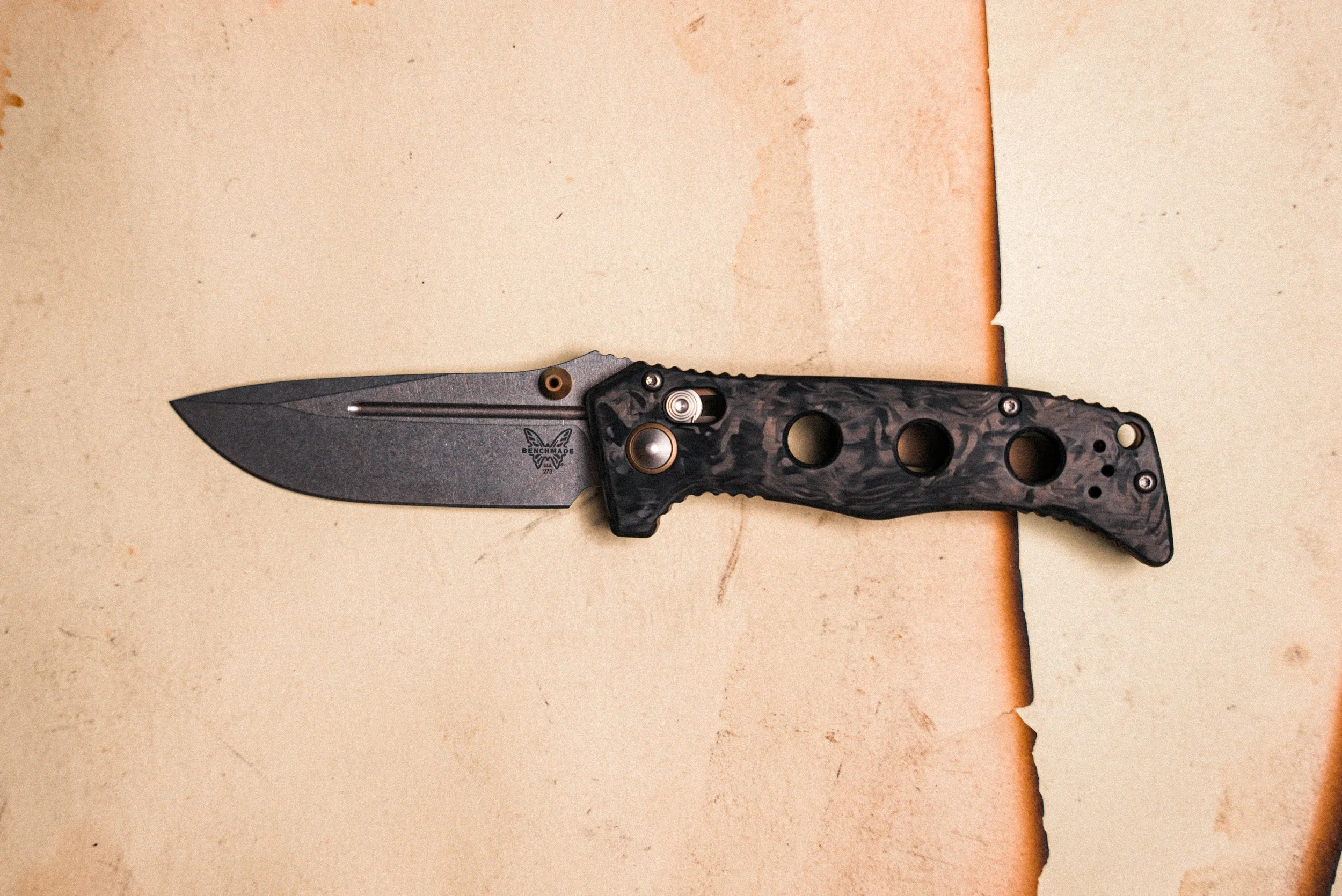 A folding pocket knife with a black and gray marbled handle and a black blade, lying on a beige surface.