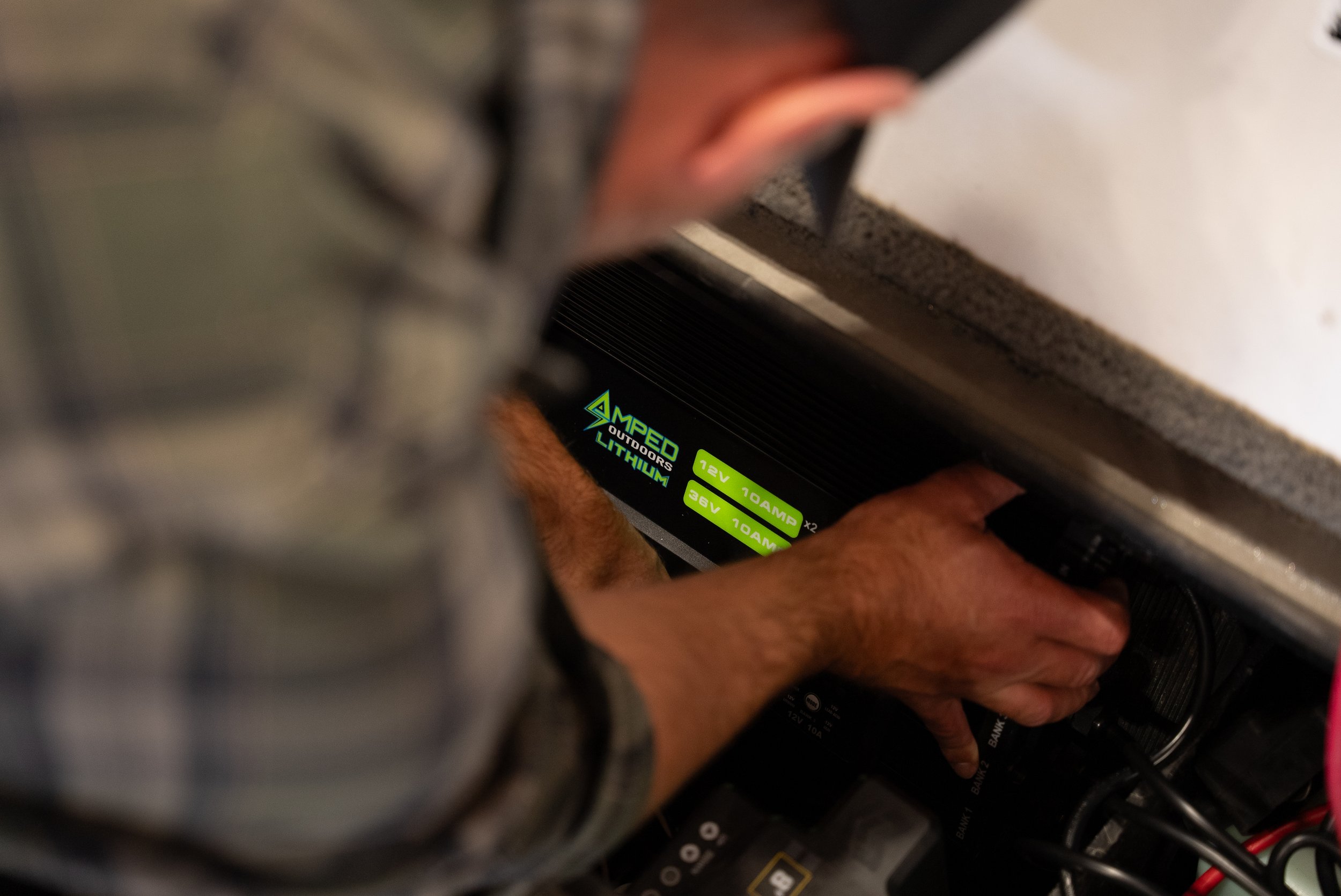 Hands installing or adjusting a lithium battery labeled 'AMED Outdoors Lithium' with voltage and amperage specifications.
