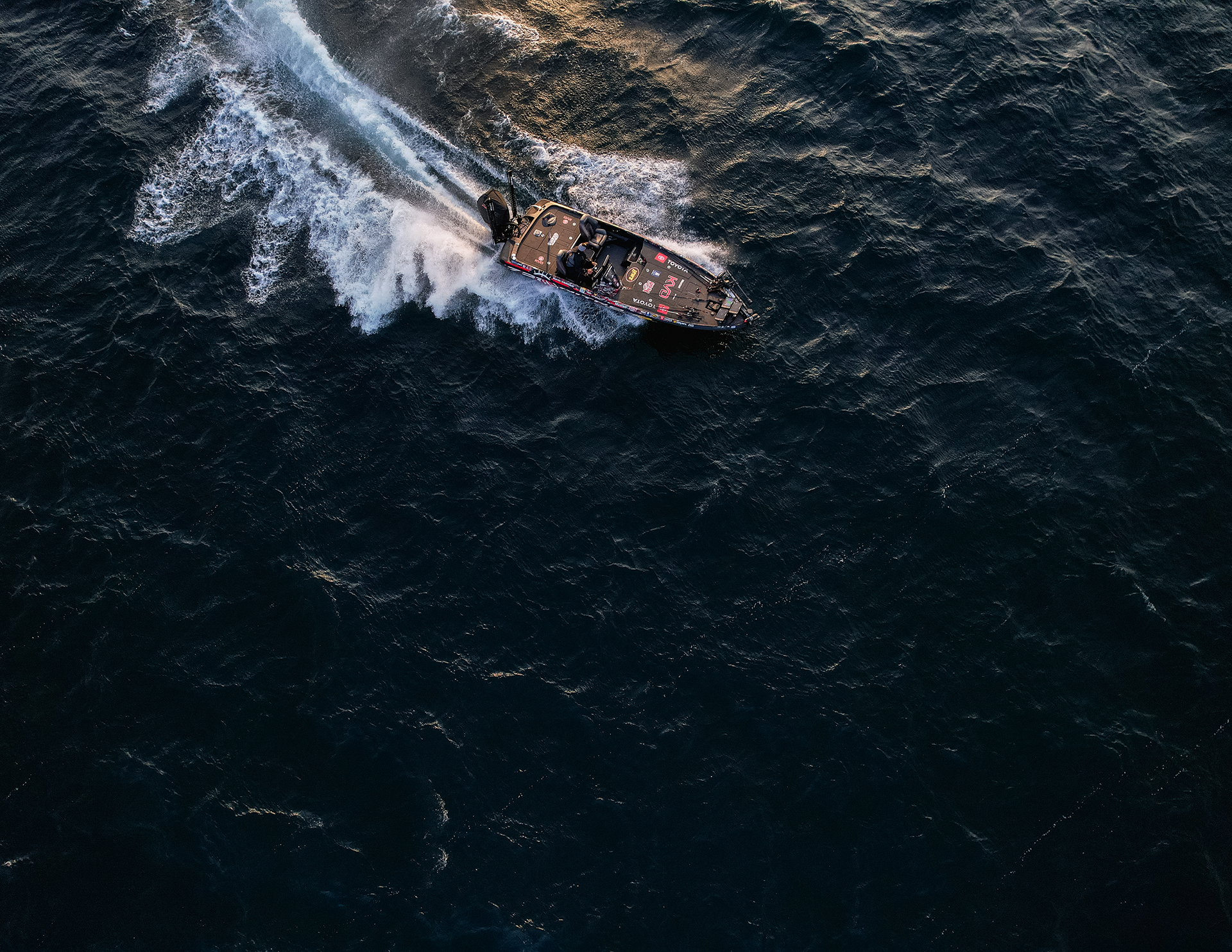 An aerial view of a boat speeding through dark water, creating a white wake behind it.