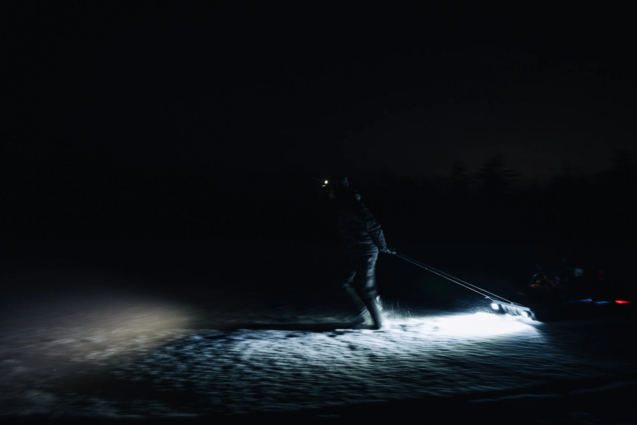 Person snowkiting at night with headlamp, pulling a kite in the snow.