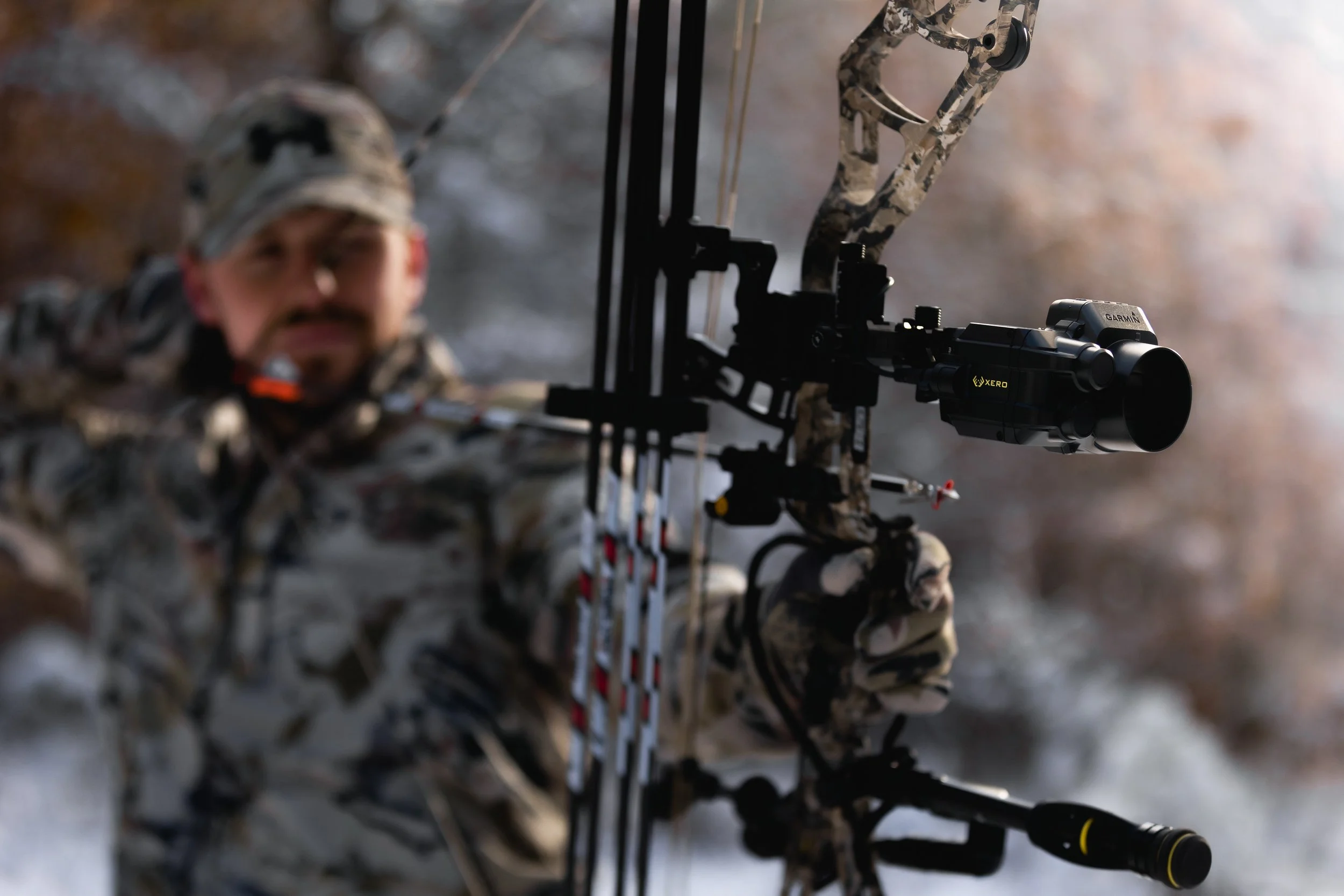 A hunter in camouflage clothing aiming a crossbow with a scope in a forest setting.